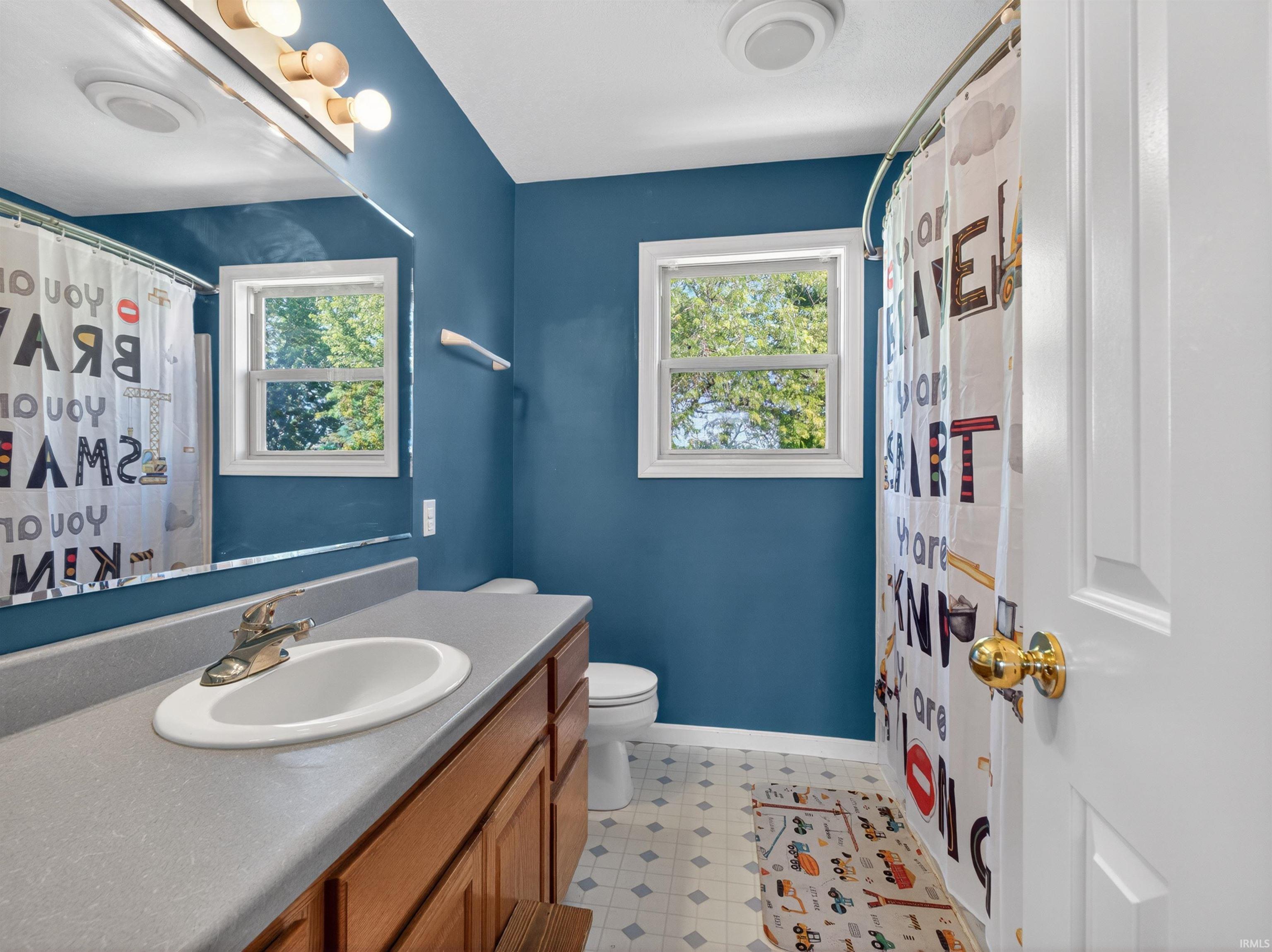 Bathroom featuring a wood-finish vanity with an integrated sink and gray countertop, a large wall mirror, and a window providing natural light