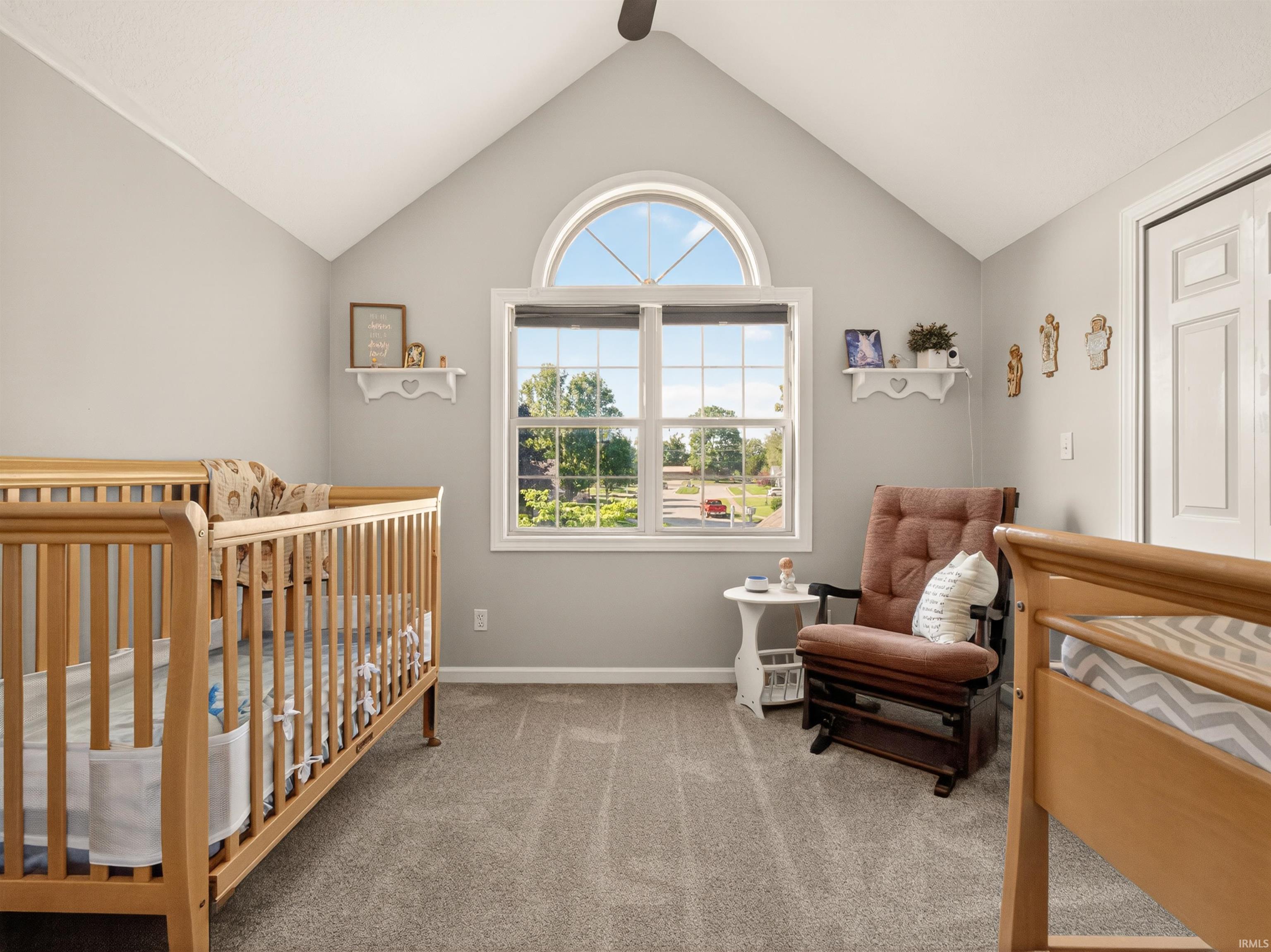 Vaulted ceiling room featuring a large arched window, light gray wall paint, and gray carpet flooring
