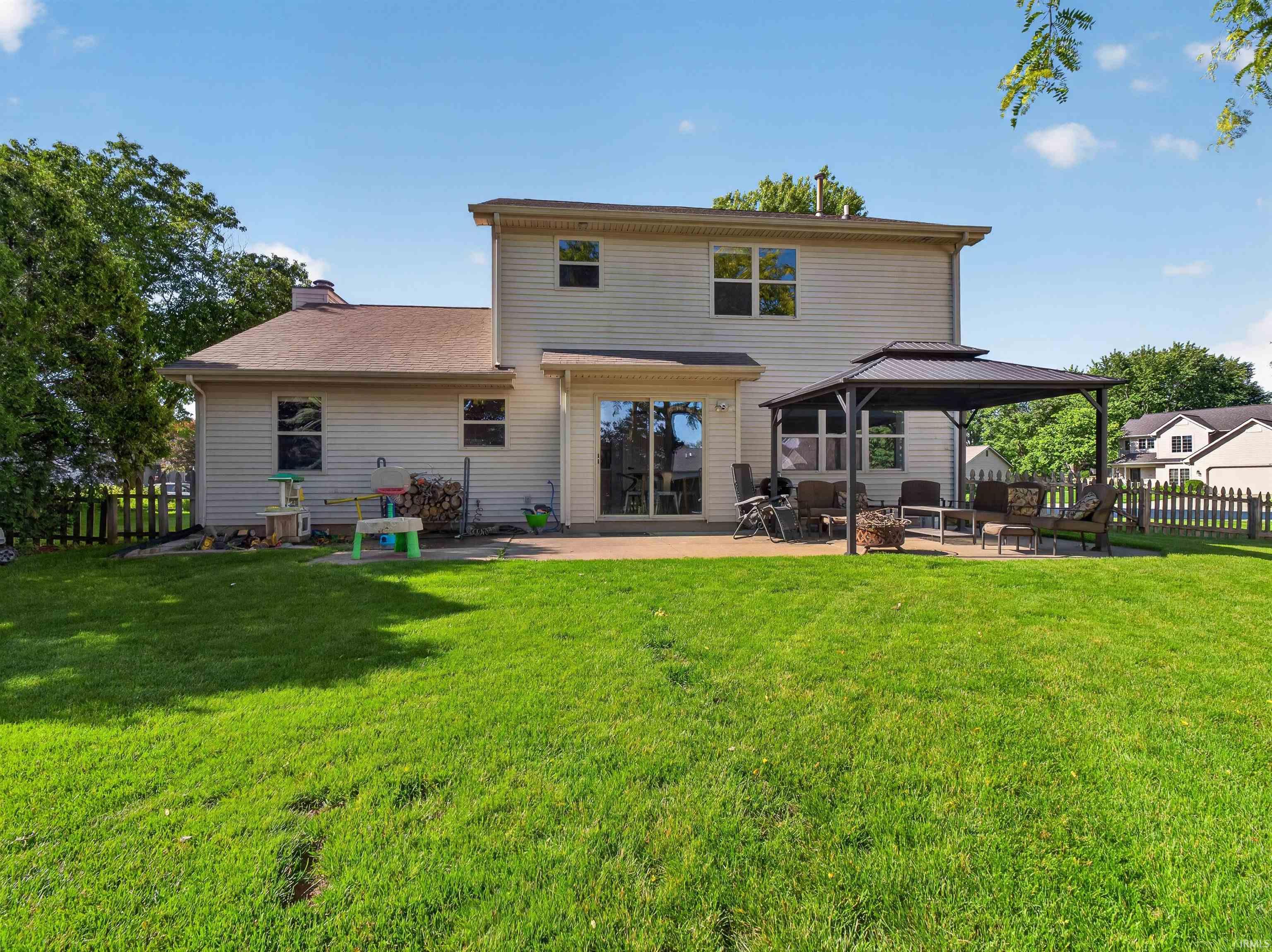 Expansive backyard featuring a large green lawn, concrete patio, and a privacy fence