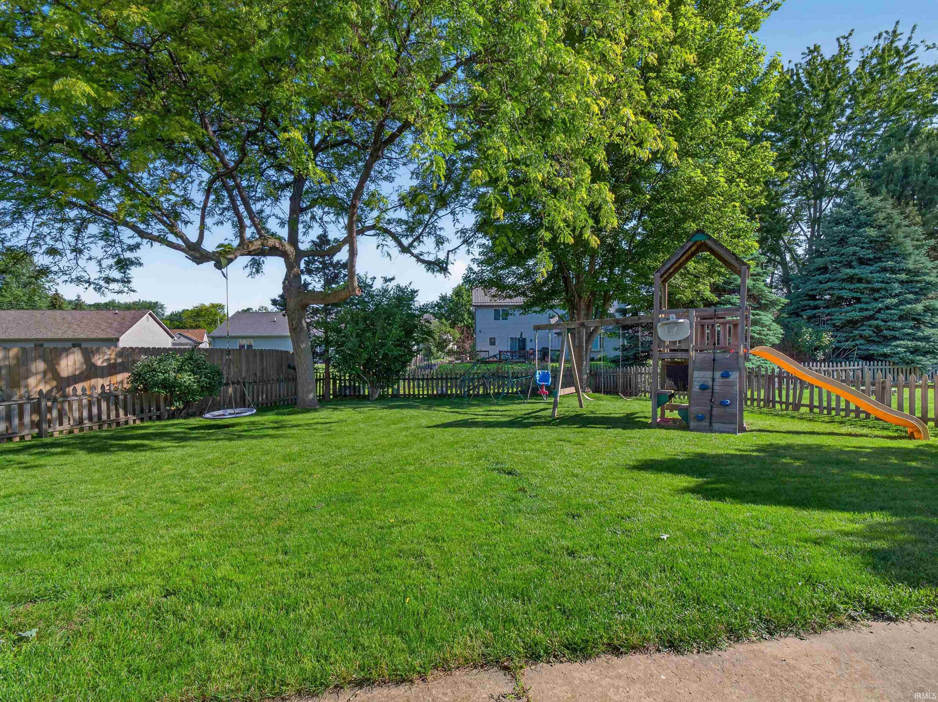 Spacious fenced backyard featuring a substantial lawn area, mature trees, and a wooden picket fence