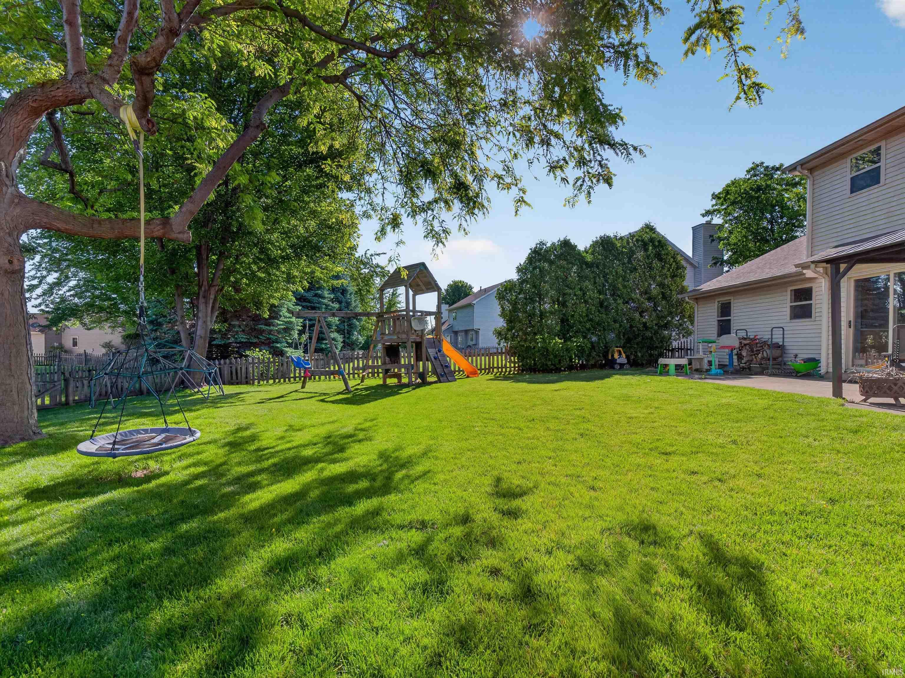 Expansive backyard featuring a large green lawn, mature trees, and a wooden privacy fence
