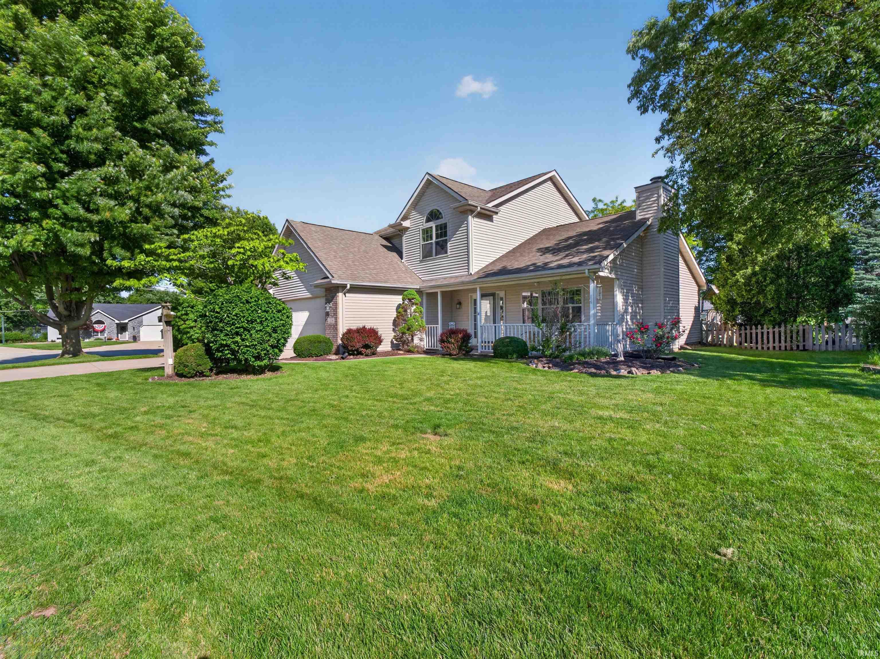 Two-story residence featuring light-toned siding, a covered front porch with white railings, a prominent chimney, and an attached two-car garage