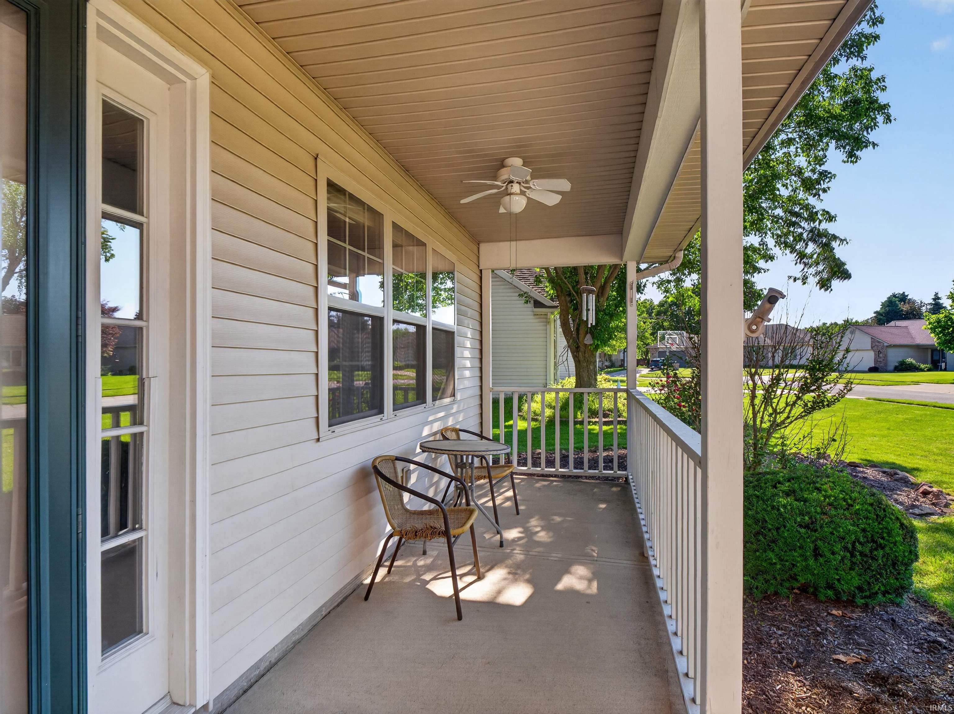 Covered front porch featuring a ceiling fan, white paneled siding, multiple transom windows, and a concrete floor