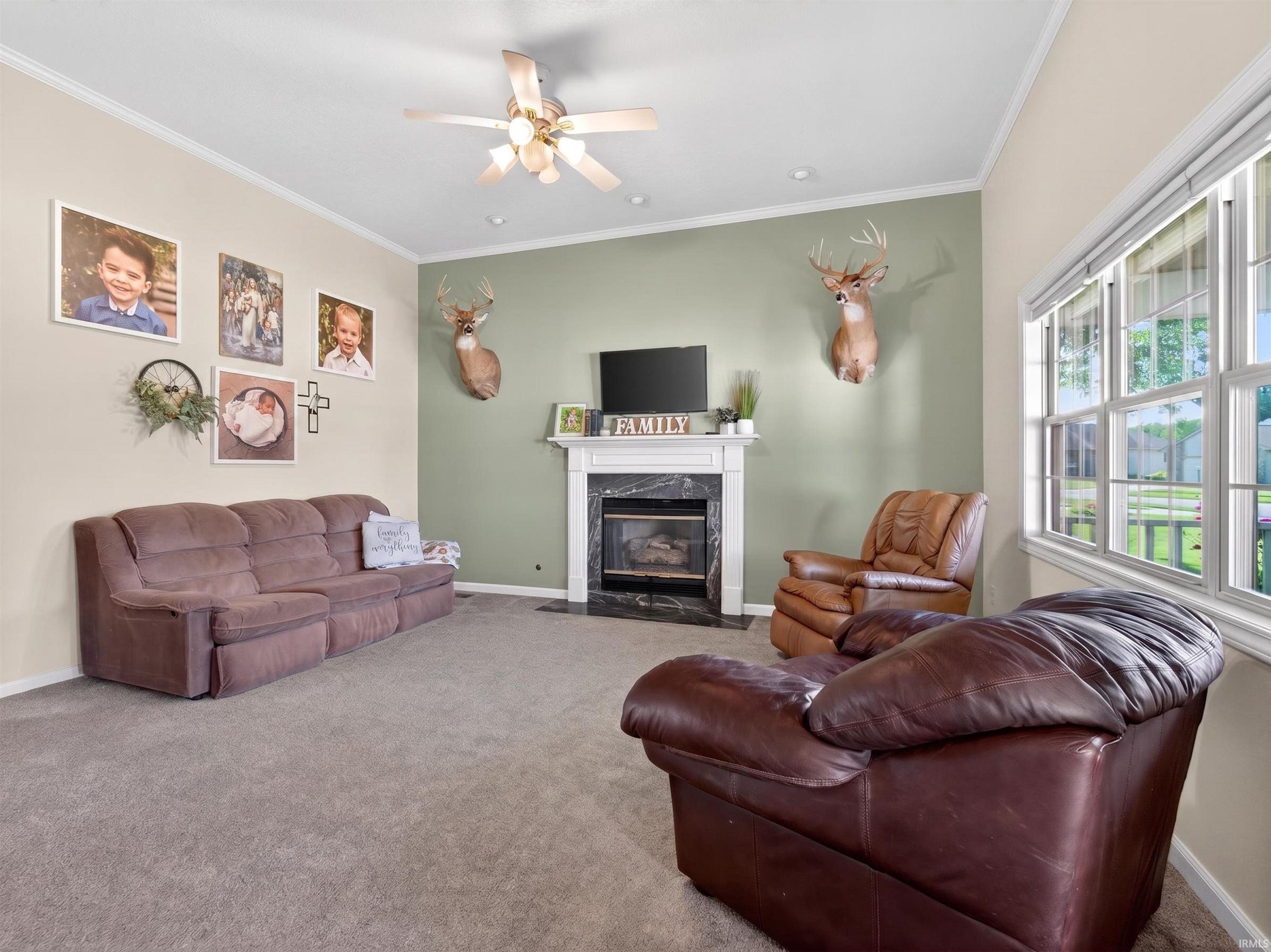Living area featuring a fireplace with a white mantel and dark surround, recessed lighting, crown molding, and a ceiling fan