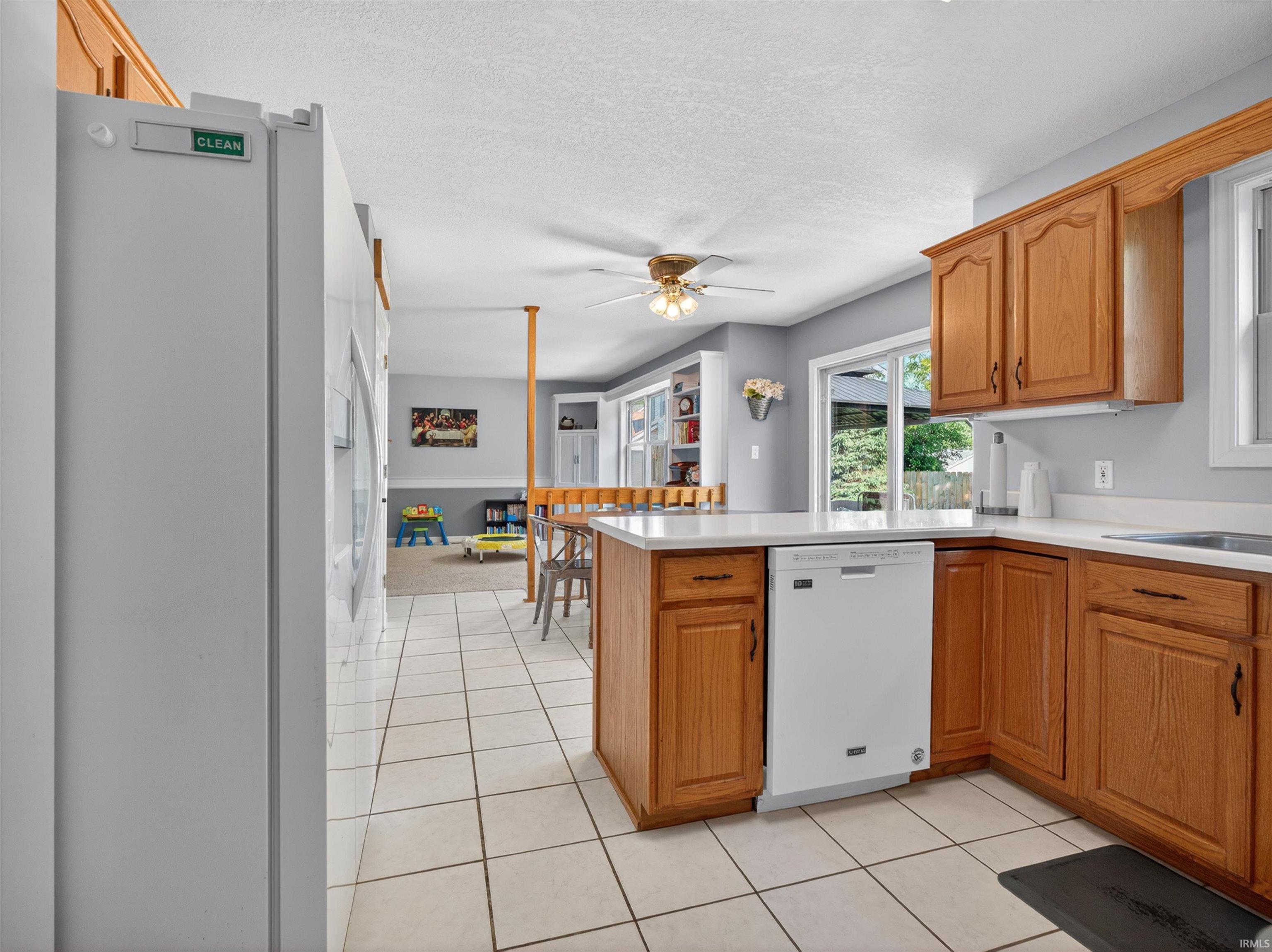 Kitchen featuring wood cabinetry, light-toned countertops, a built-in dishwasher, and tile flooring