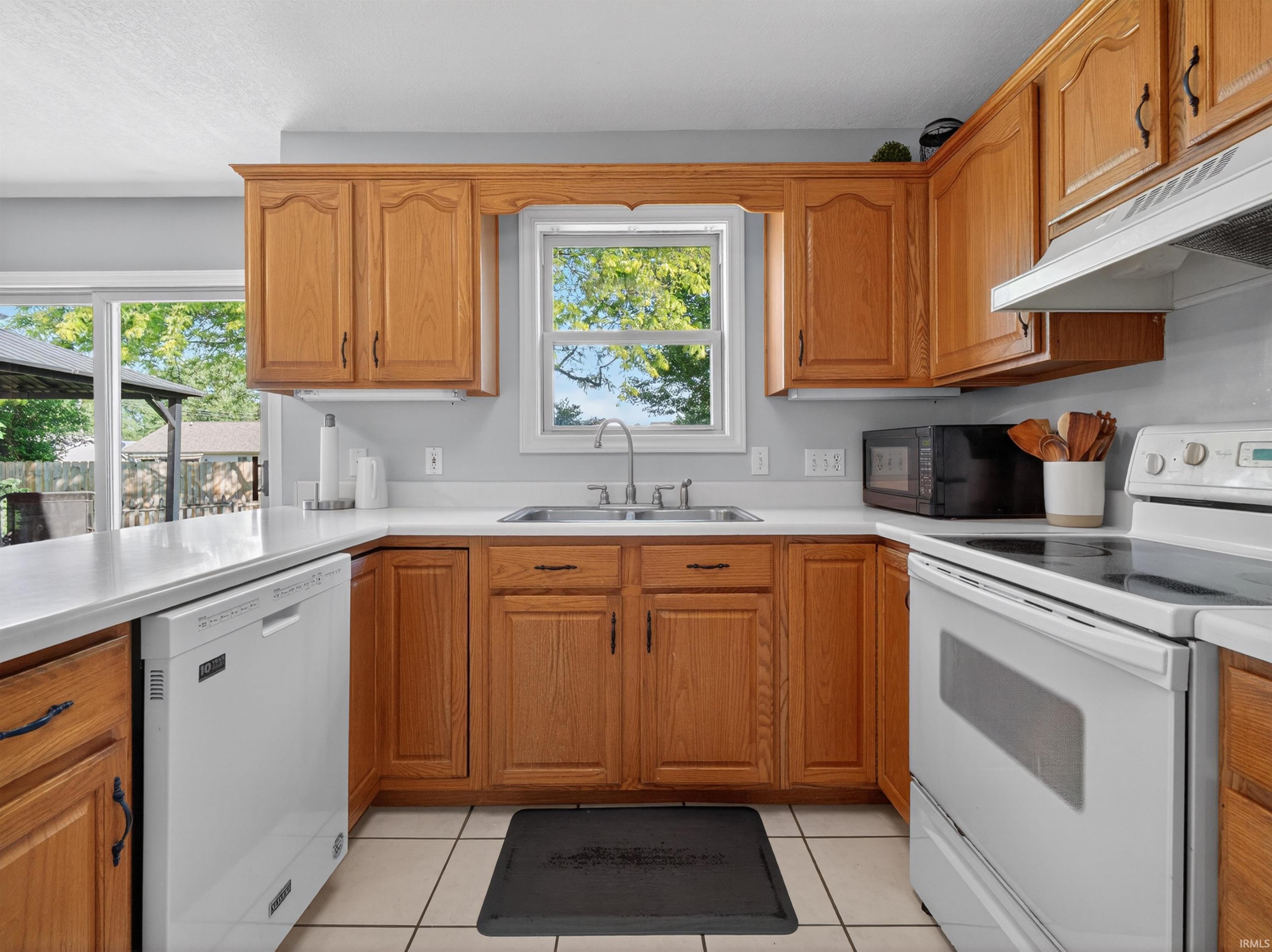 Kitchen featuring wood cabinetry, white countertops, tile flooring, and a stainless steel sink with a window