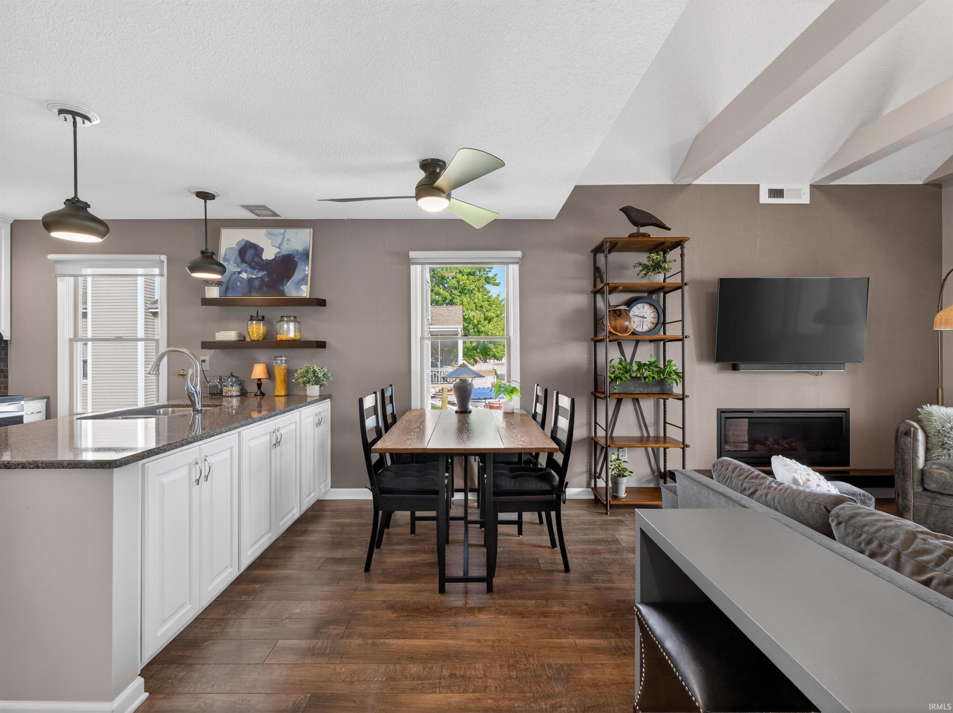 Open-concept living space featuring wood-finish flooring, a kitchen island with white cabinetry and granite-style countertops, and pendant lighting