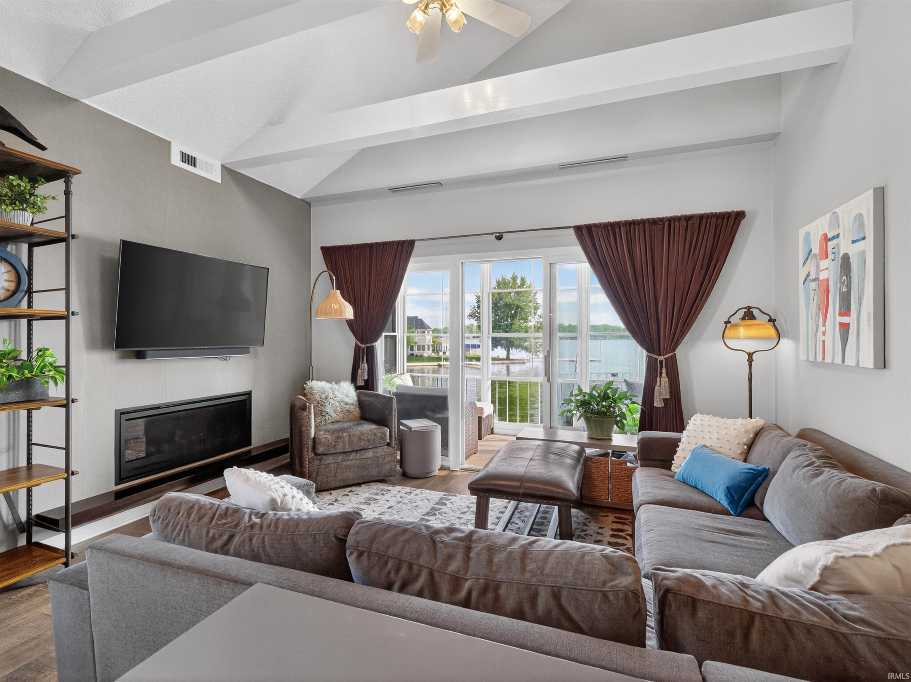 Living area featuring vaulted ceilings with exposed beams, a built-in electric fireplace, wood-finish flooring, and a glass sliding door opening to an outdoor space