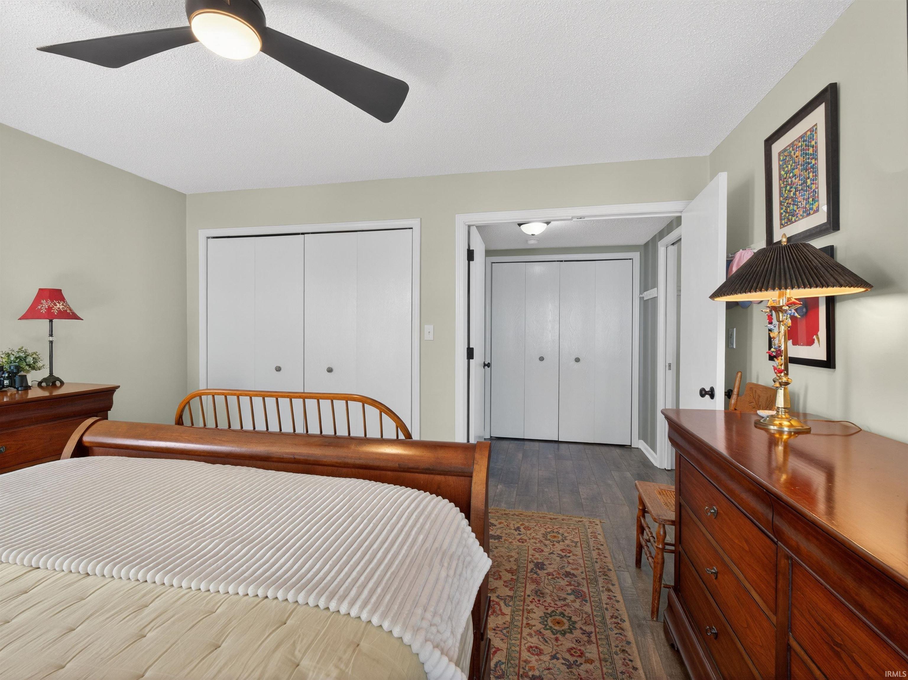 Spacious bedroom featuring multiple closets, a ceiling fan with integrated lighting, and wood-finish flooring extending into the hallway