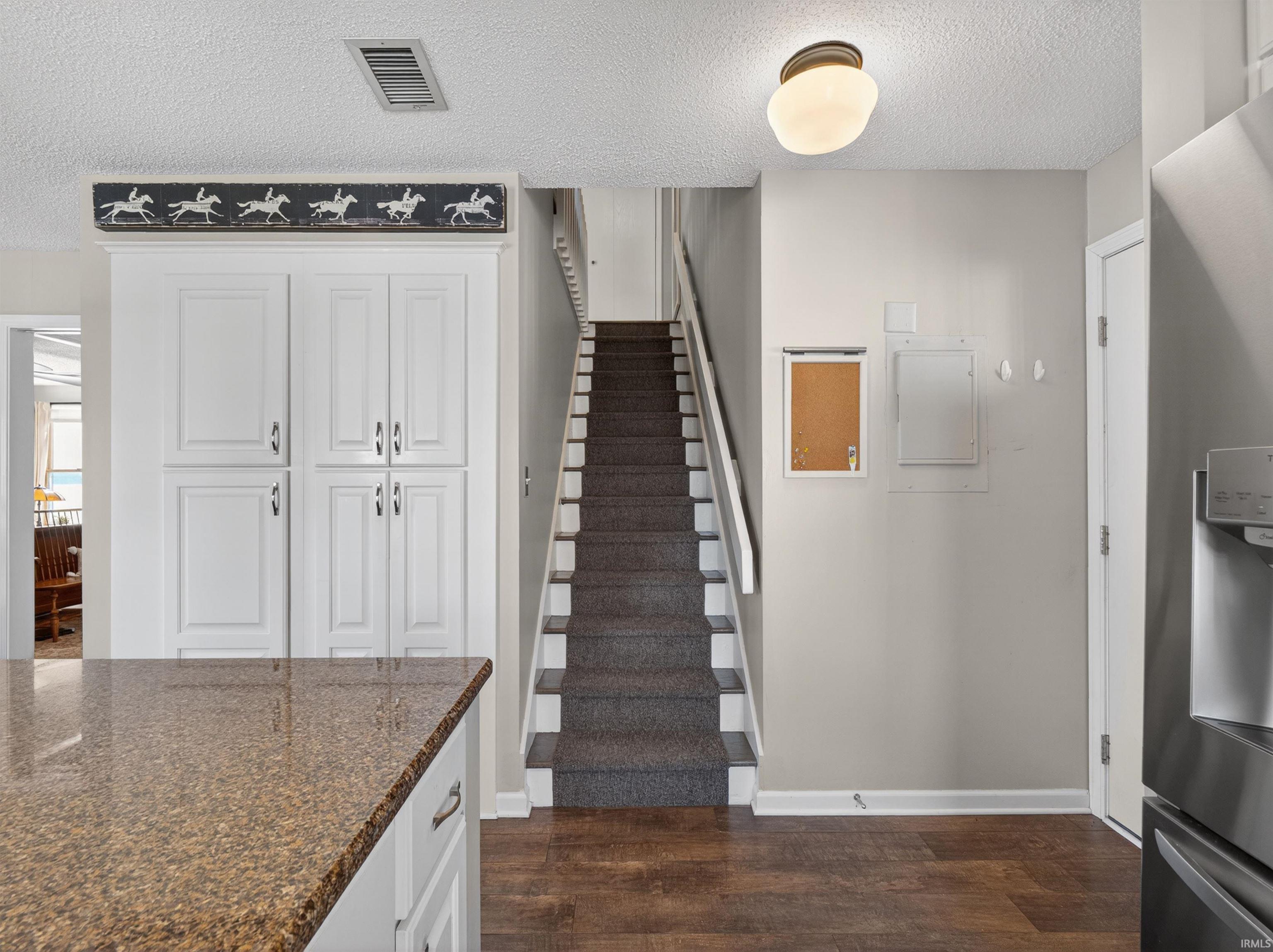 Kitchen area featuring white cabinetry, a speckled countertop, dark wood-finish flooring, and a carpeted staircase with white risers