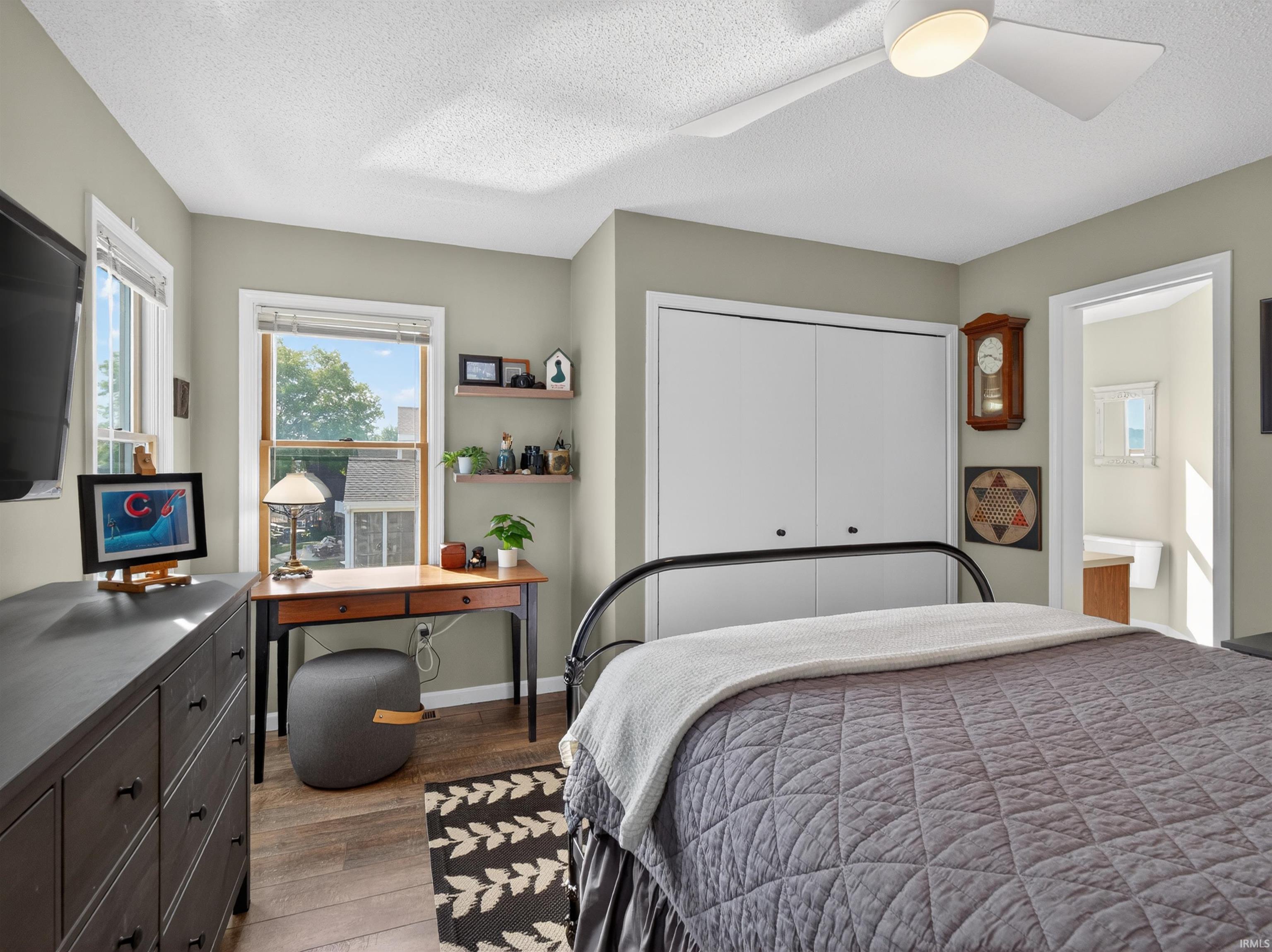 Light-filled room featuring wood-finish flooring, two windows with white trim, and a white ceiling fan