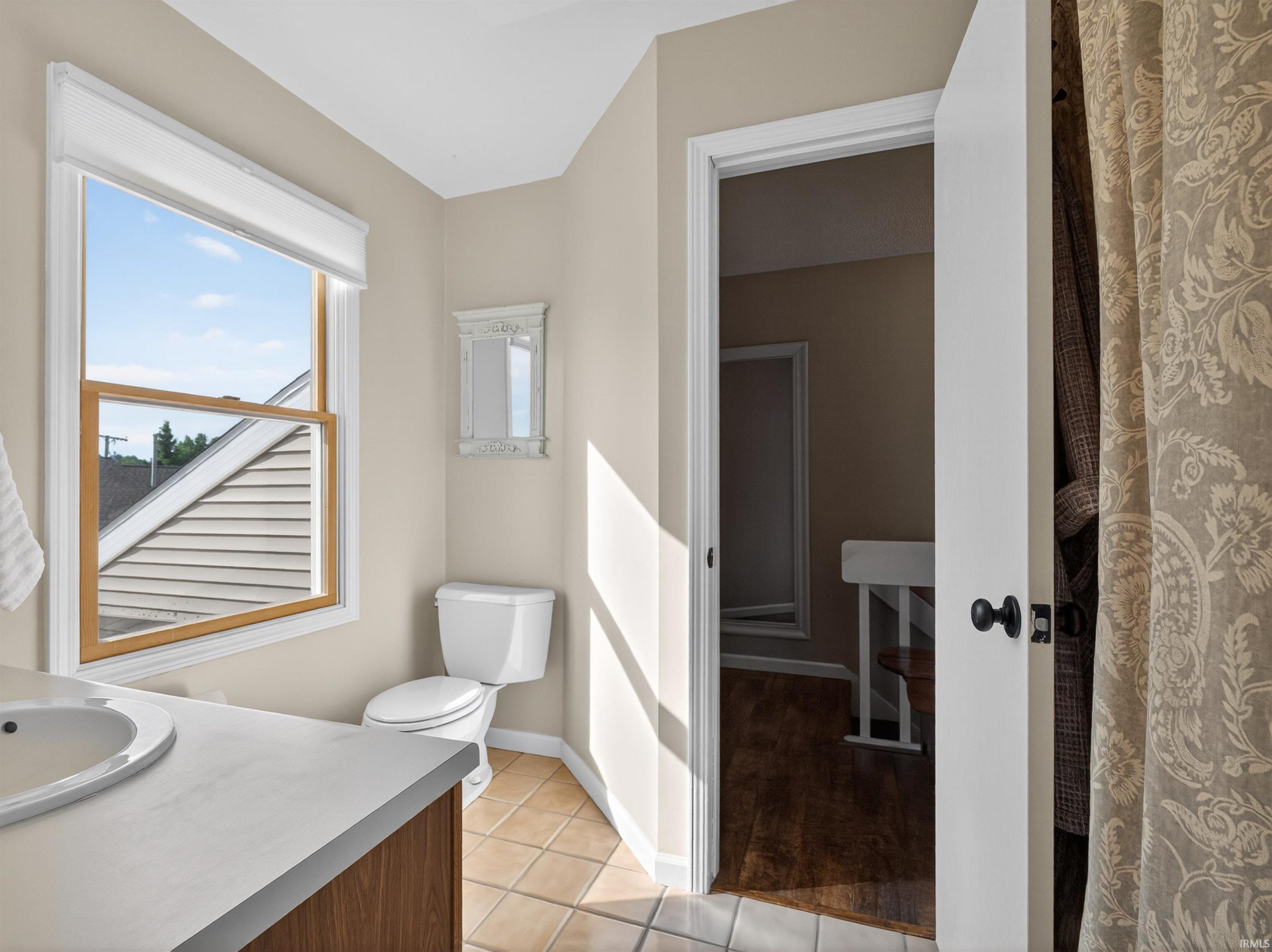 Bathroom featuring a single-pane window, white toilet, tile flooring, and a vanity with an integrated sink