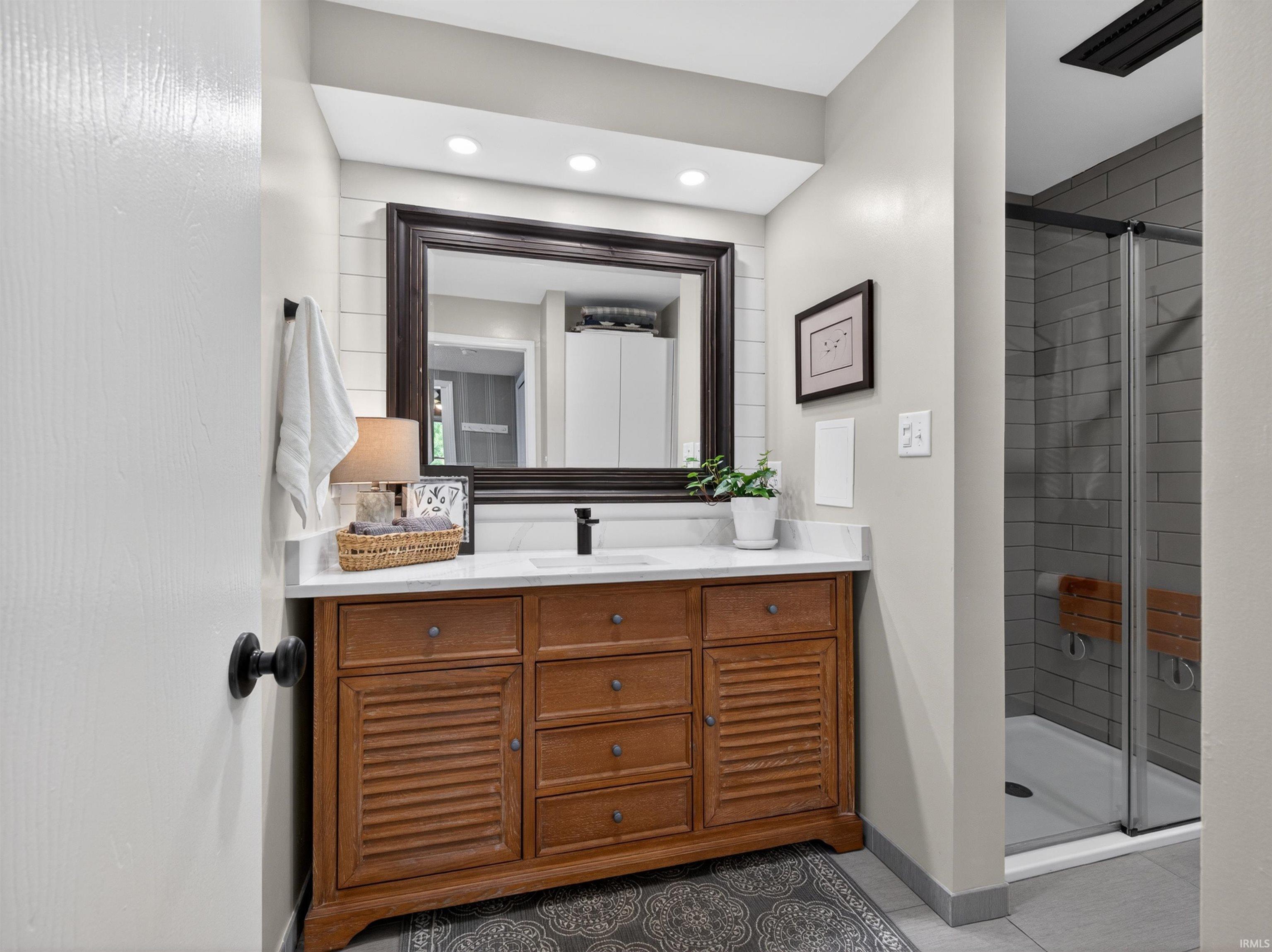 Bathroom featuring a wood-finish vanity with louvered doors, a white countertop, and a dark framed mirror