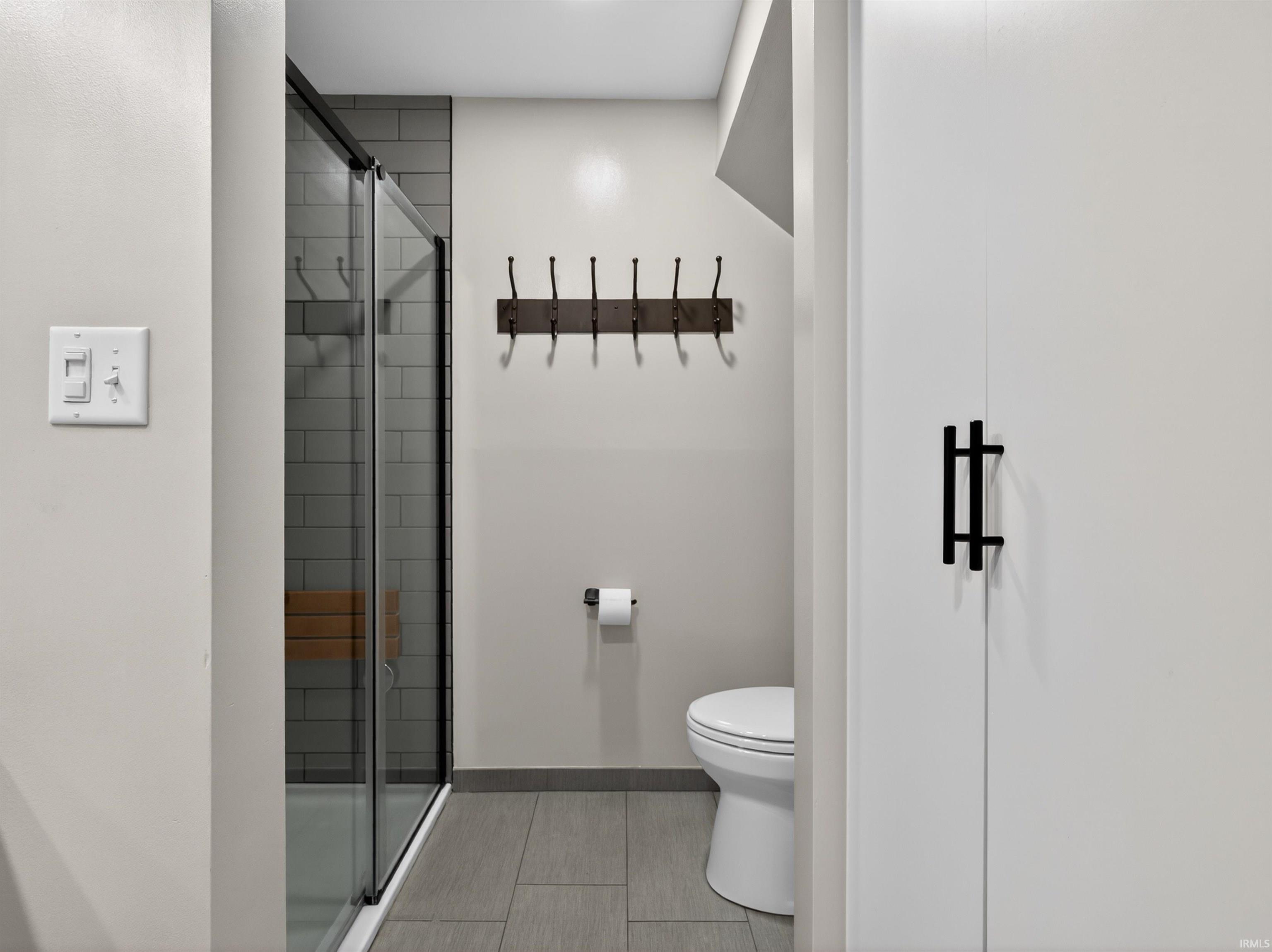 Bathroom featuring a glass-enclosed shower with subway tile, a mounted wooden shower bench, and a modern toilet