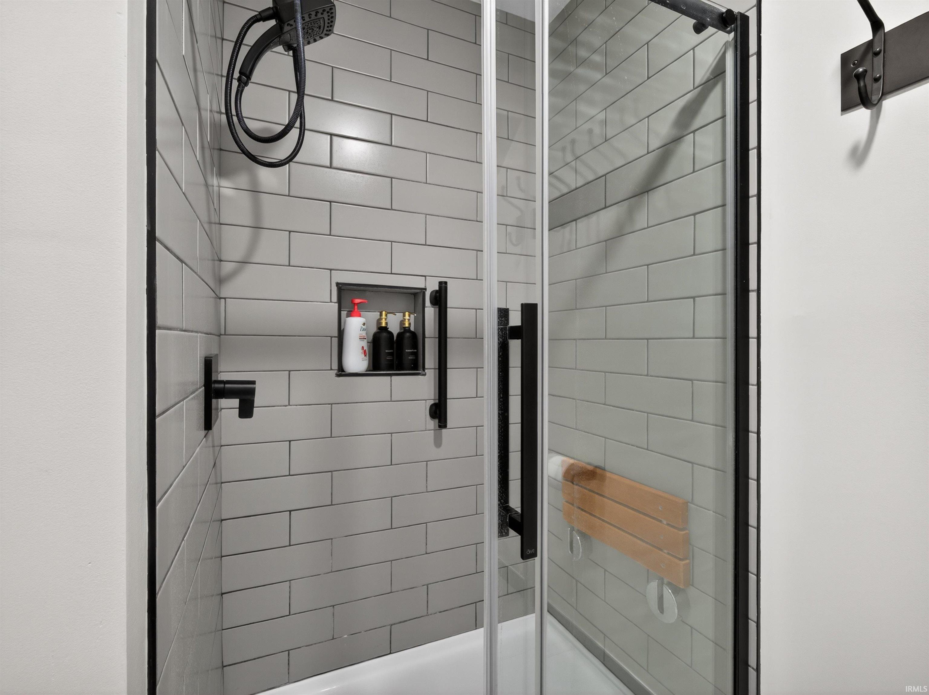 Enclosed shower with subway tile surround, black-framed glass door, and matte black fixtures