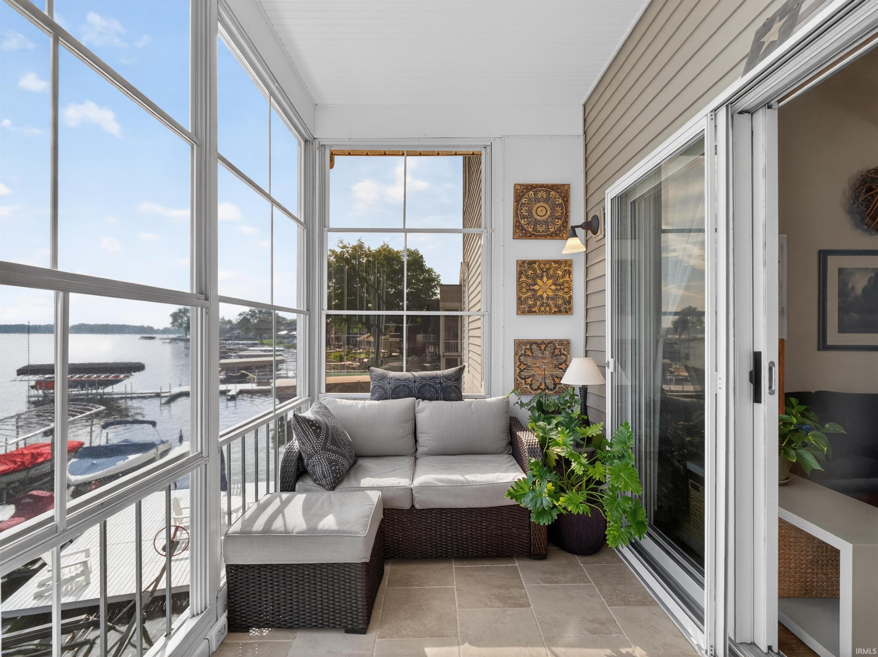 Enclosed sunroom featuring expansive windows, a water body with docks, sliding glass doors, a ceiling fan, and tile flooring
