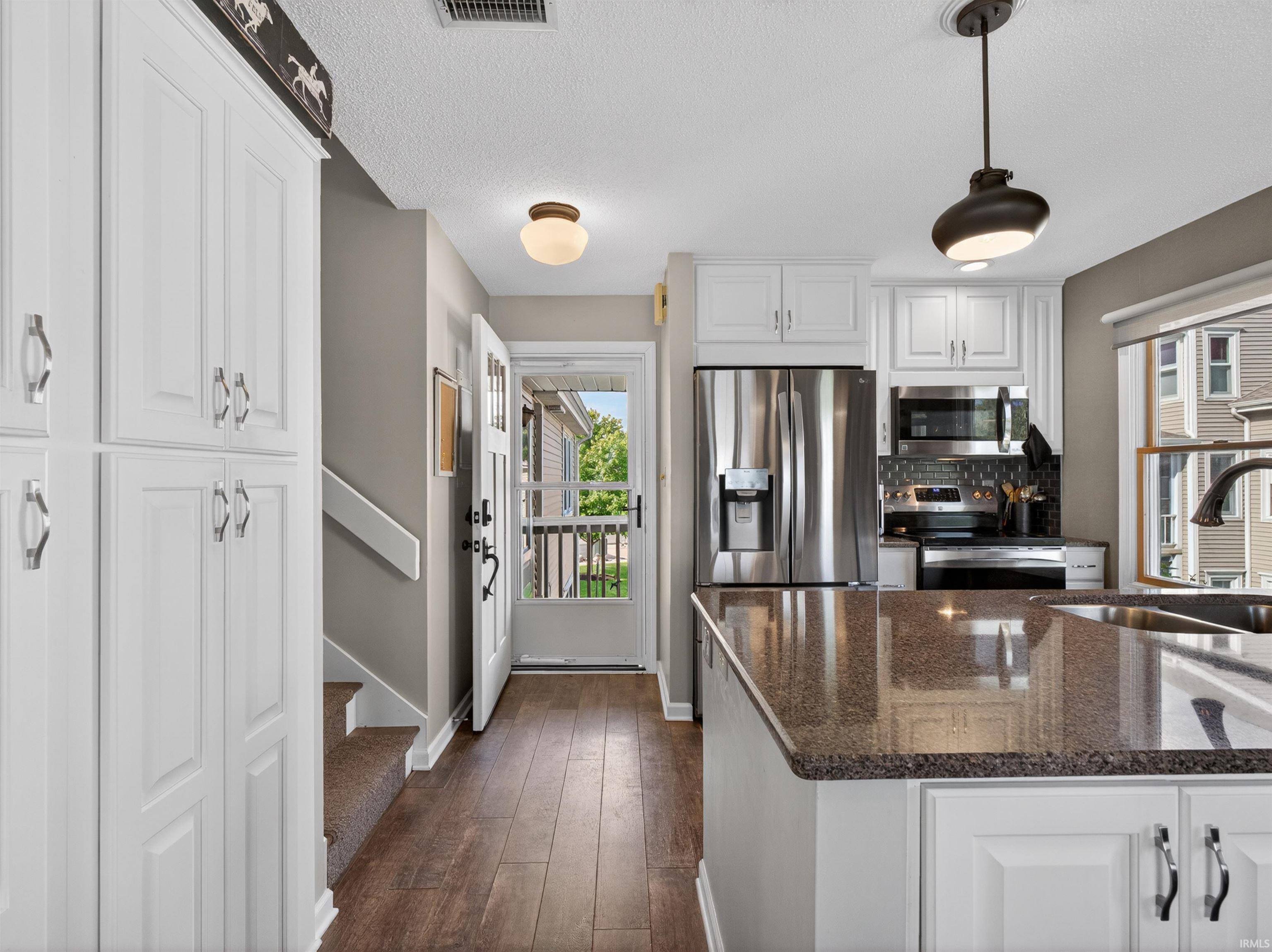 Kitchen featuring white cabinetry, stainless steel appliances, a dark granite-finish island with an undermount sink, and wood-finish flooring