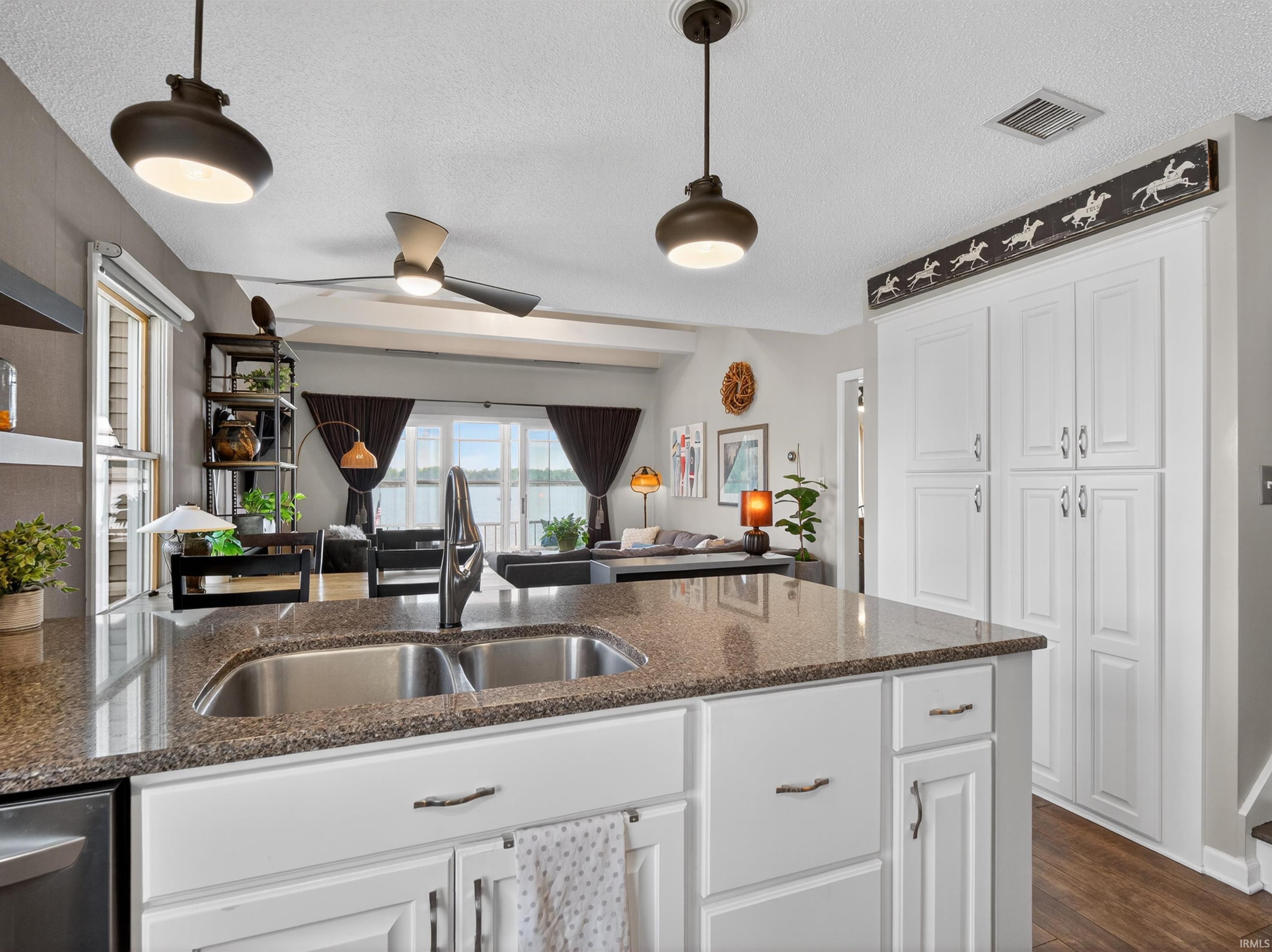 Kitchen island featuring a double basin stainless steel sink, granite-finish countertop, and white cabinetry with dark hardware