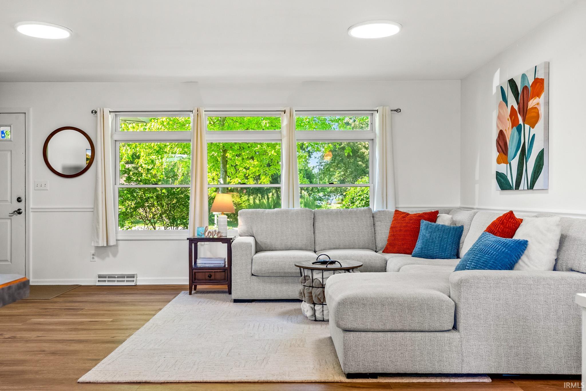 Light-filled living area featuring wood-finish flooring, white walls, and a trio of large windows