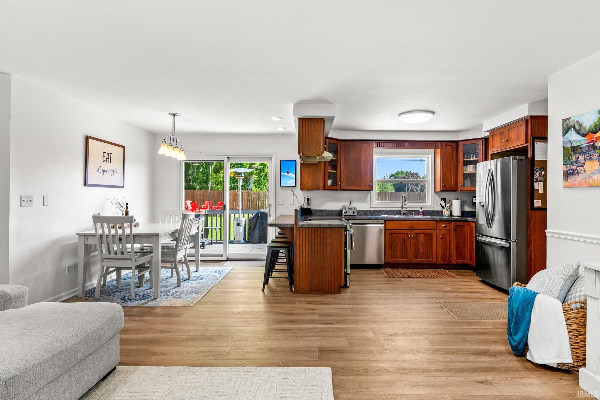Open-concept living space featuring wood-finish flooring throughout, a kitchen with wood cabinetry and stainless steel appliances, and a dining area with a contemporary chandelier