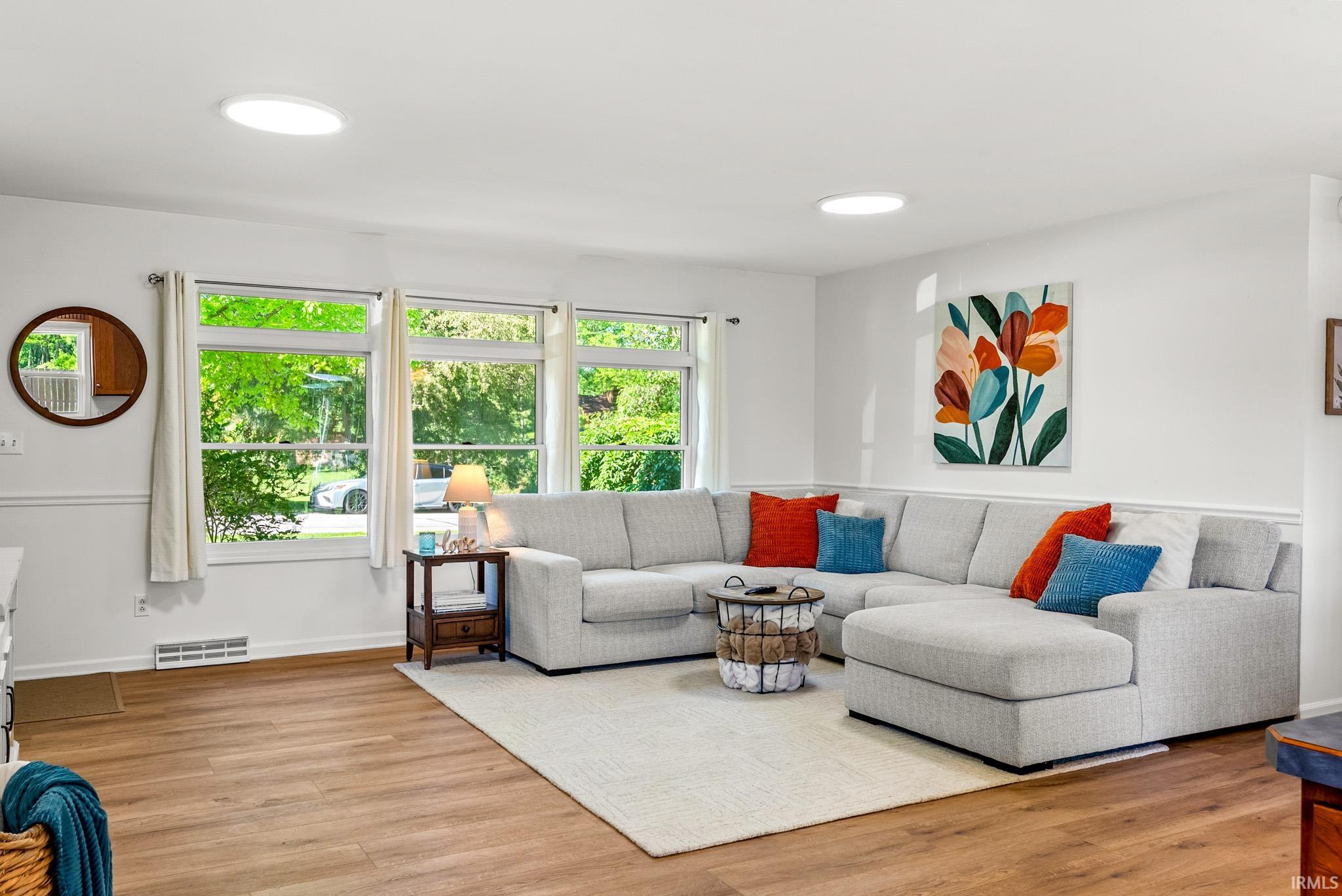 Spacious living area featuring expansive windows, wood-finish flooring, two circular ceiling lights, and white wall paneling