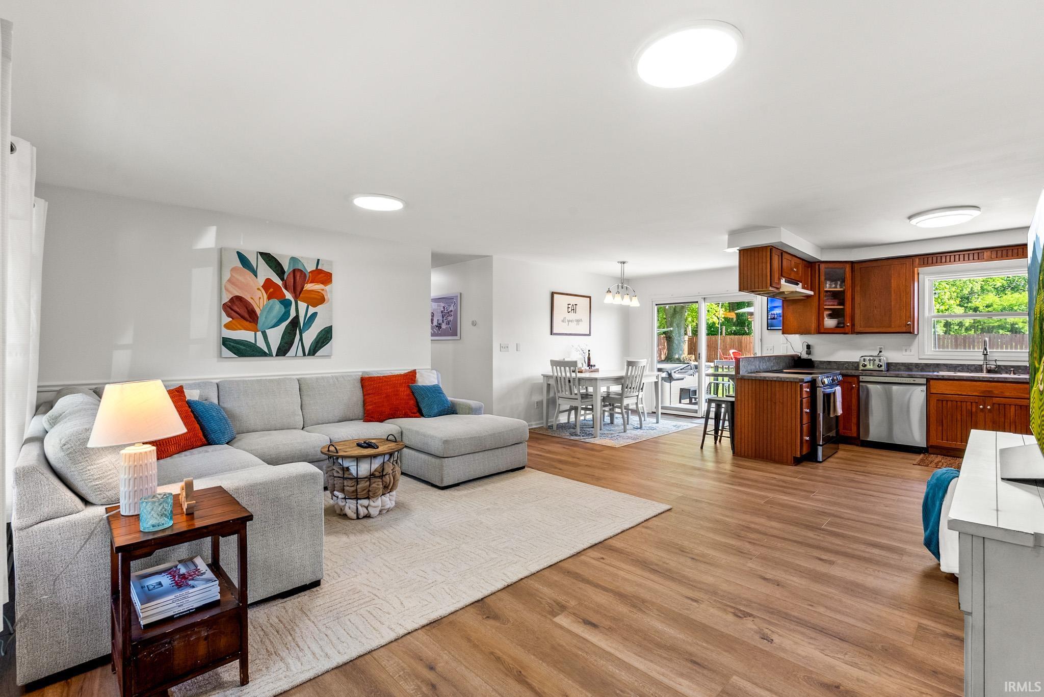 Open-concept living area featuring wood-finish flooring, recessed lighting, and a kitchen with stainless steel appliances, dark wood cabinetry, and a peninsula with seating