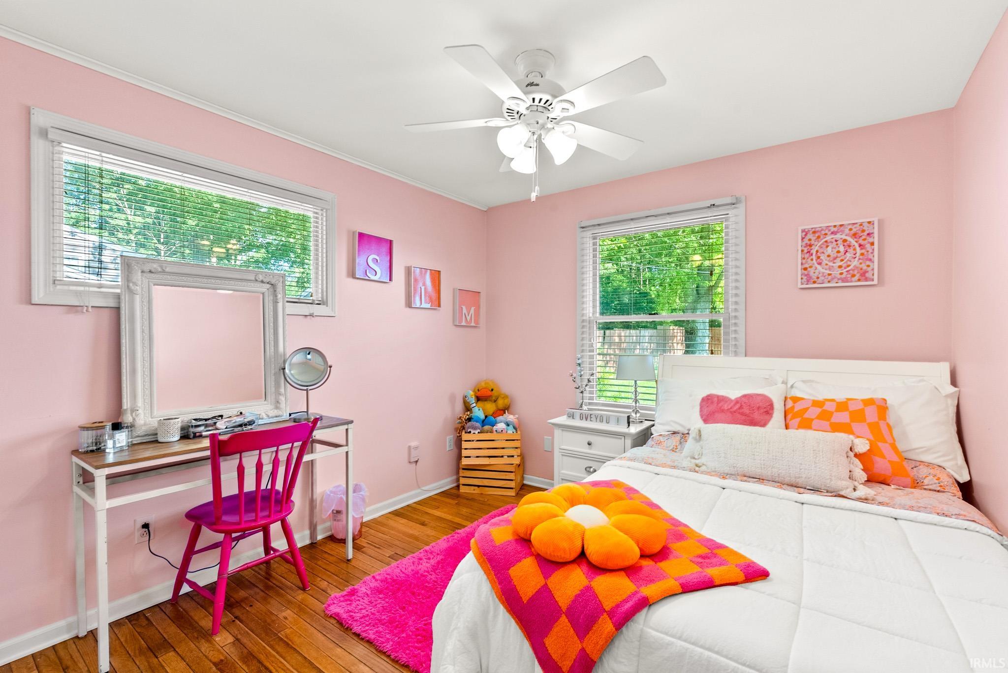 Bedroom featuring two windows with white blinds, wood-finish flooring, a white ceiling fan, and white baseboards