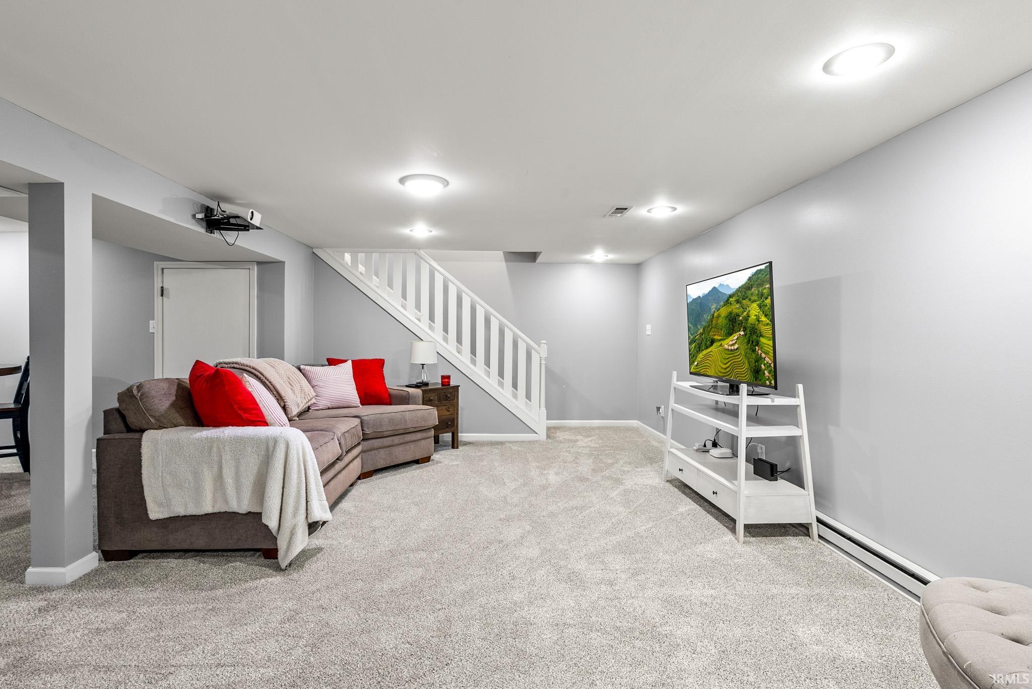 Finished room featuring light gray carpeting, recessed ceiling lighting, a white painted staircase, and neutral wall tones