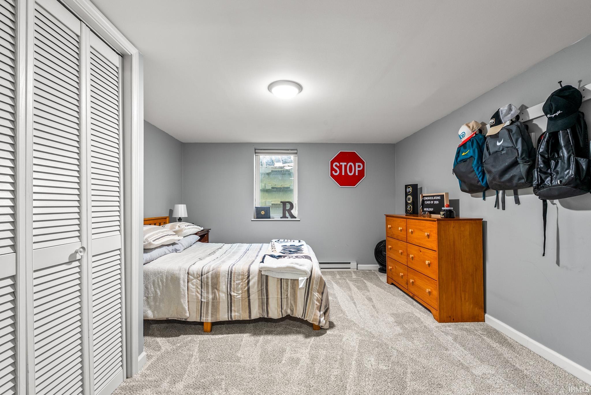 Bedroom featuring light gray walls, textured carpet flooring, a window with exterior visibility, a ceiling-mounted light fixture, and louvered bi-fold closet doors