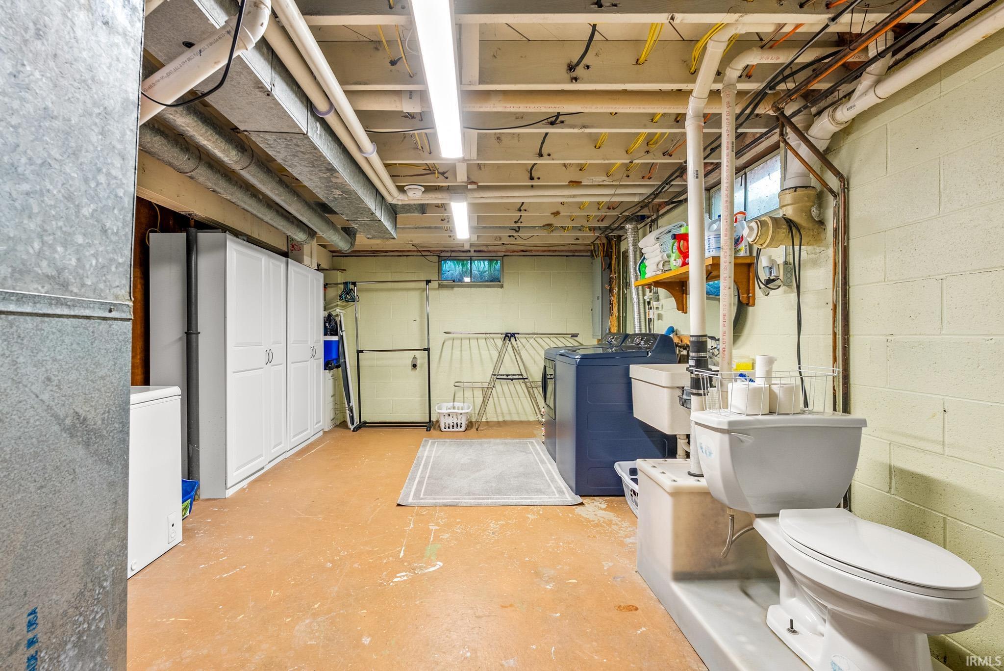 Basement utility area featuring a wall-mounted toilet, laundry sink, washing machine, and dryer