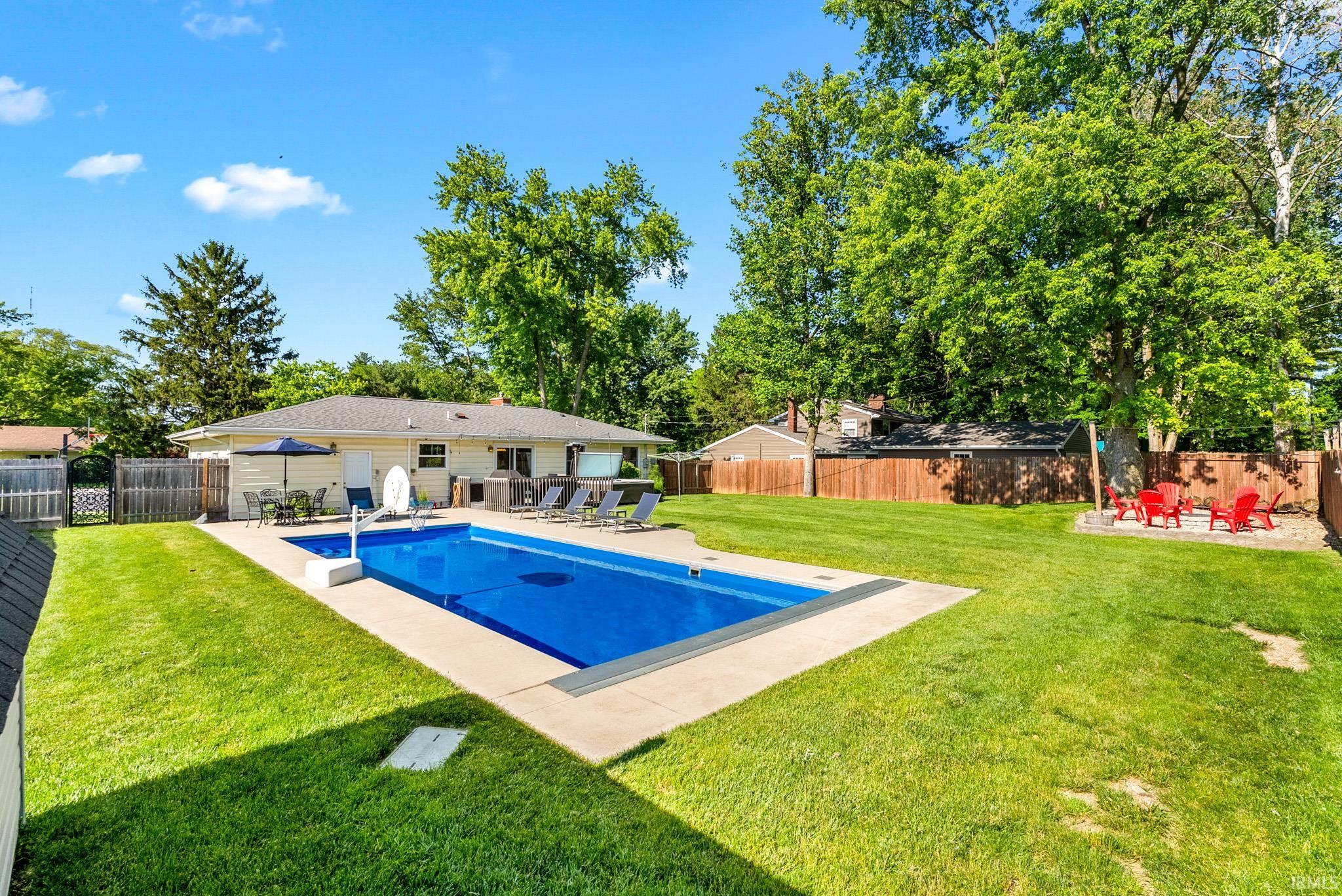 Expansive backyard featuring a rectangular in-ground pool with a concrete surround, a patio area with a dining set, a fire pit area, and a wood privacy fence