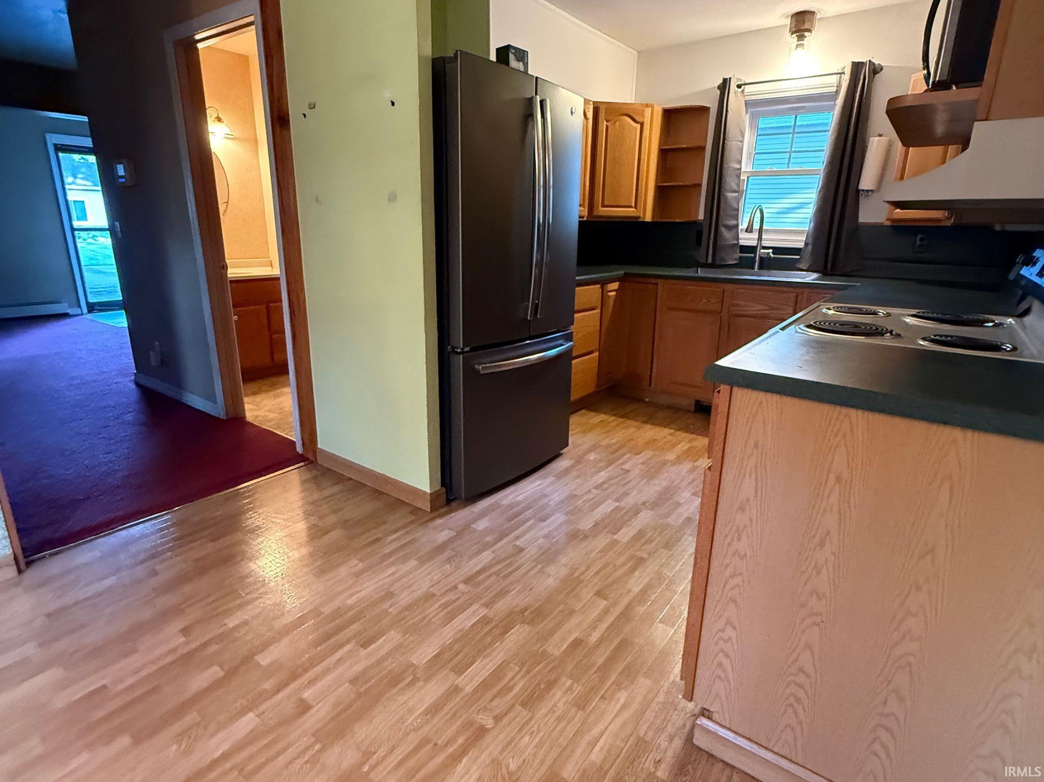Kitchen featuring wood-finish flooring, a stainless steel refrigerator, dark countertops, and wood cabinetry