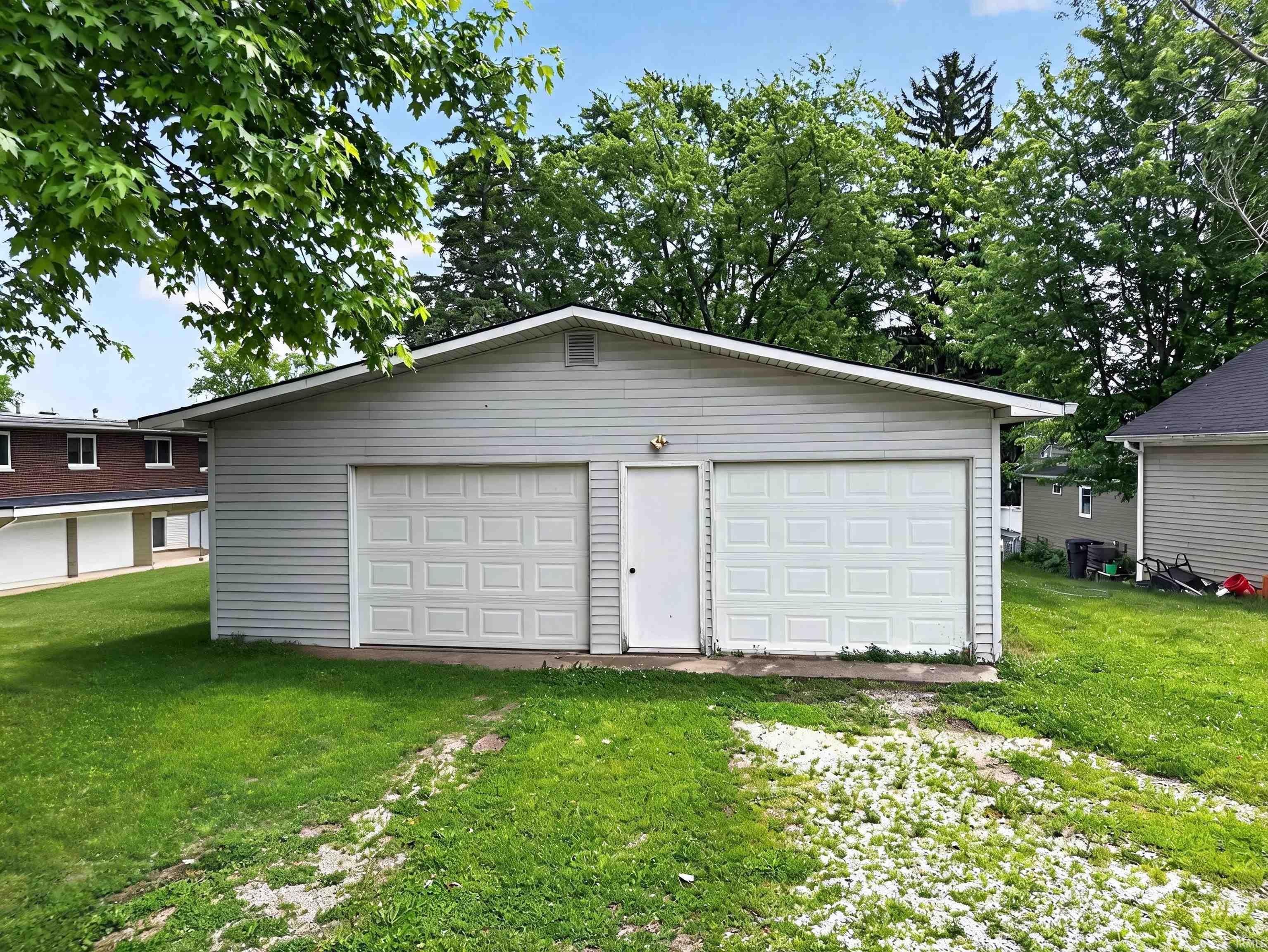 Detached garage with two overhead doors and a pedestrian entry door, featuring light gray siding and a dark shingle roof