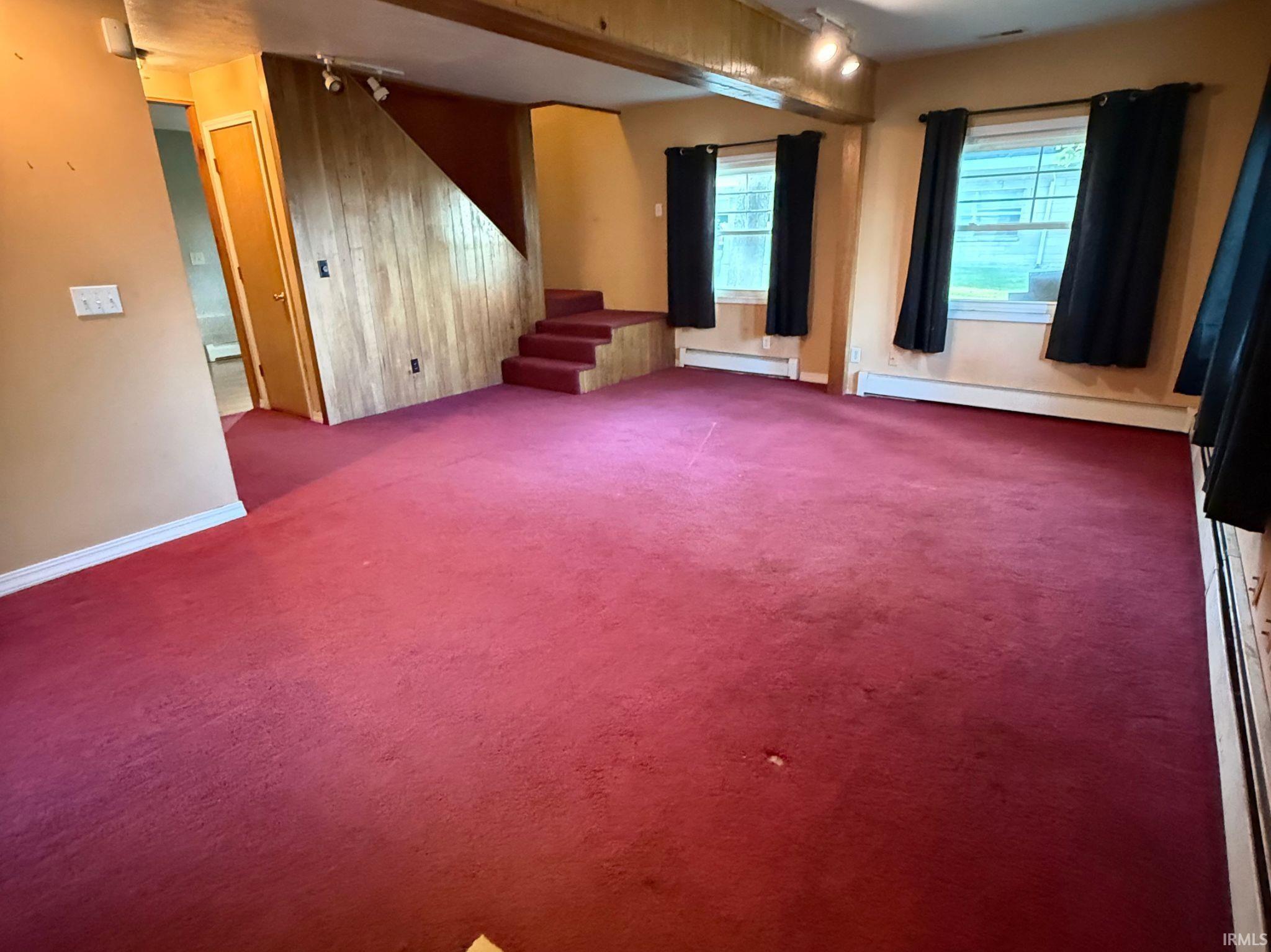 Carpeted interior space featuring wood-paneled wall accents, track lighting, and baseboard heating