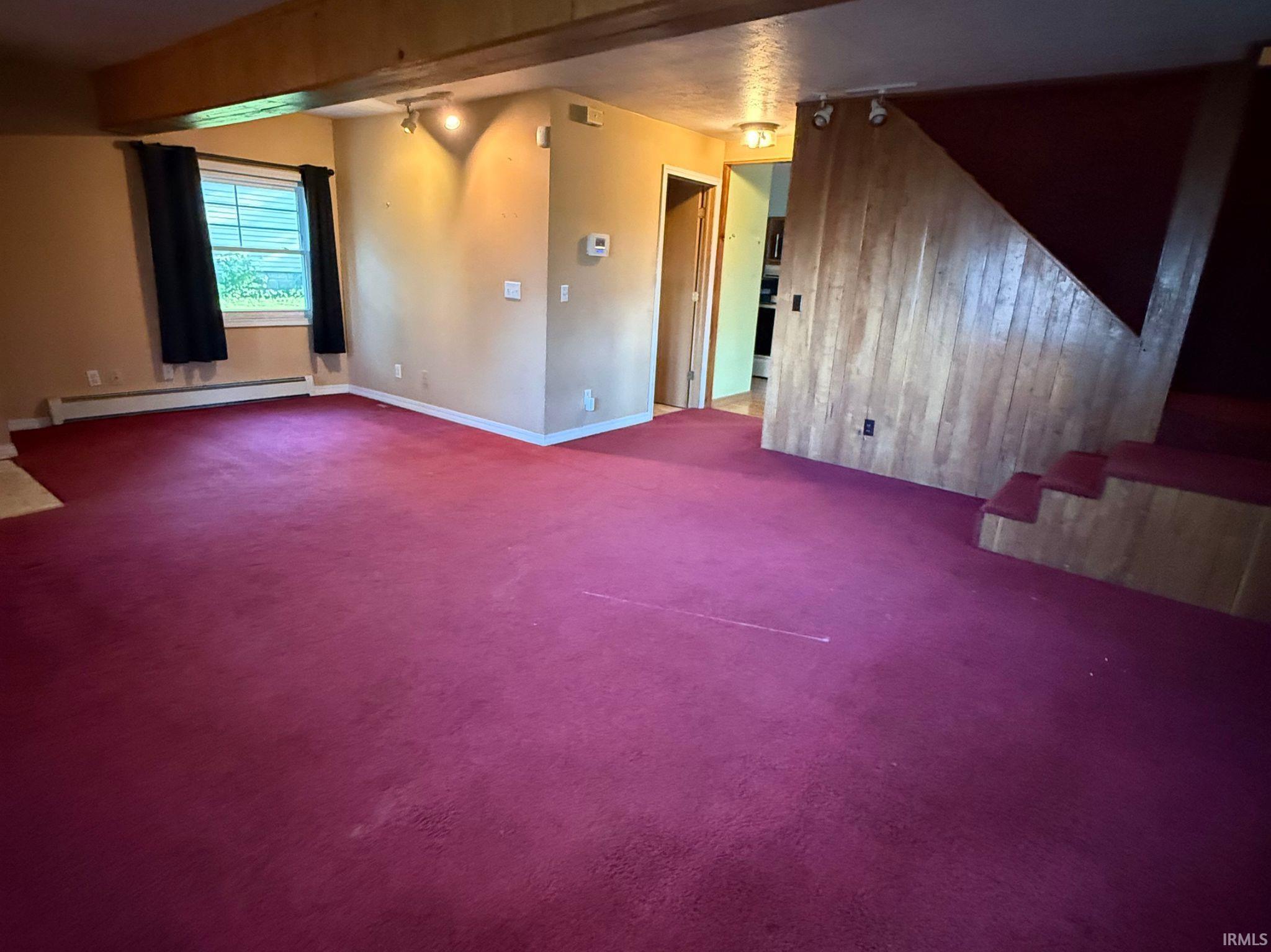 Spacious interior featuring a vibrant red carpet, exposed wood beams, and a wood-paneled staircase
