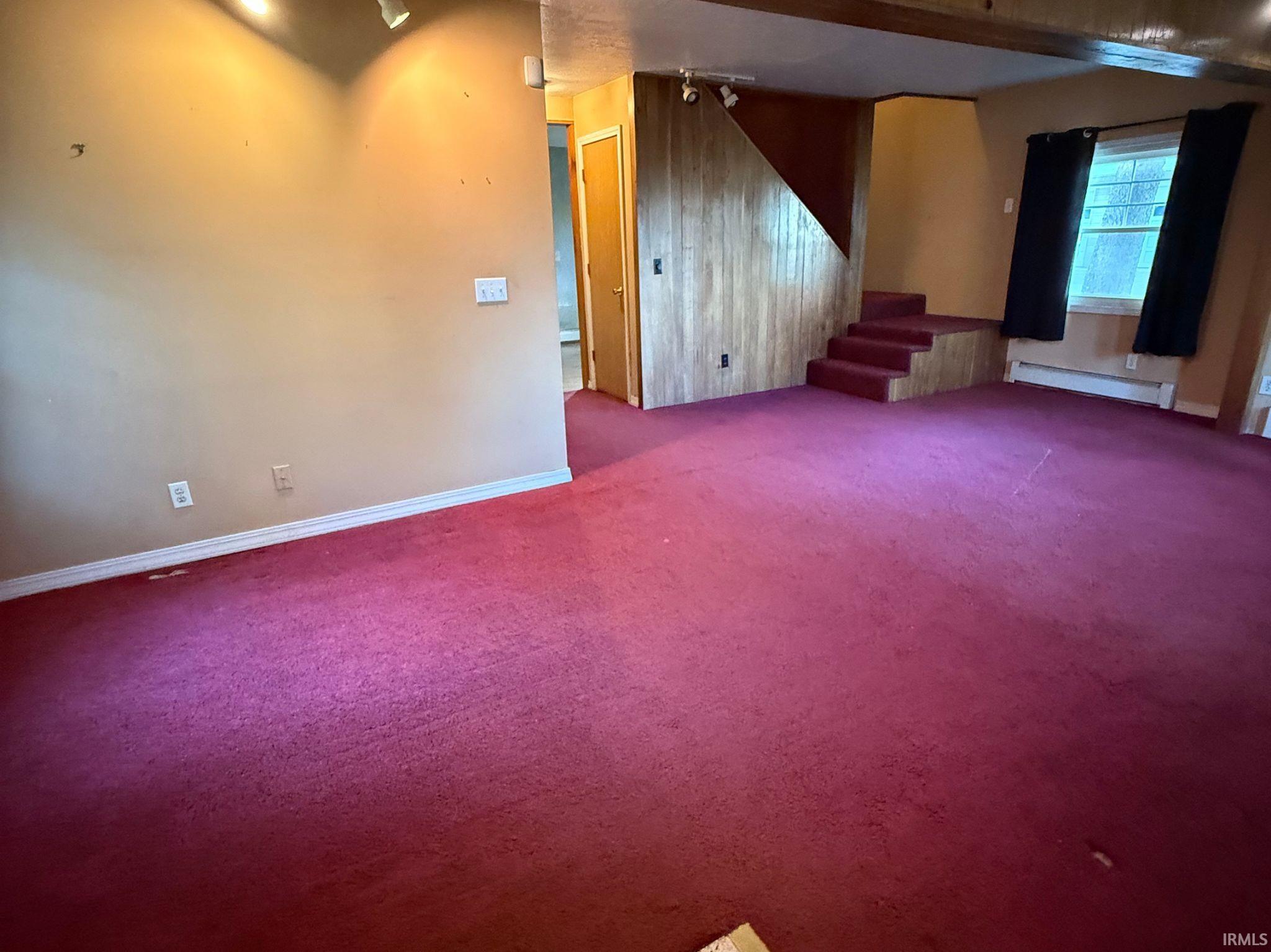 Spacious room featuring broadloom carpeting, track lighting, and a wood-paneled accent wall with integrated staircase