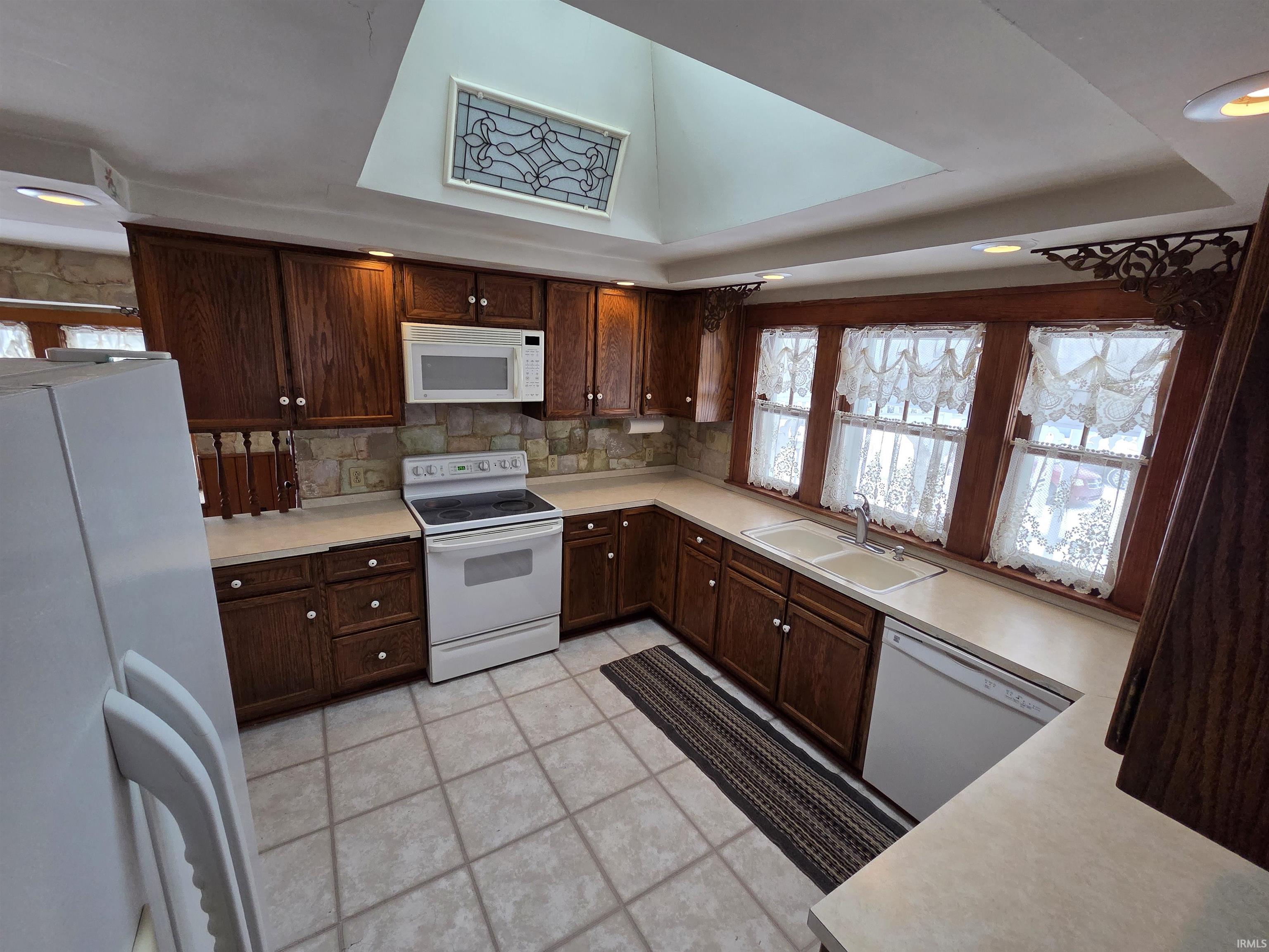 Kitchen featuring white appliances, light countertops, dark brown cabinets, decorative backsplash, and light tile patterned floors