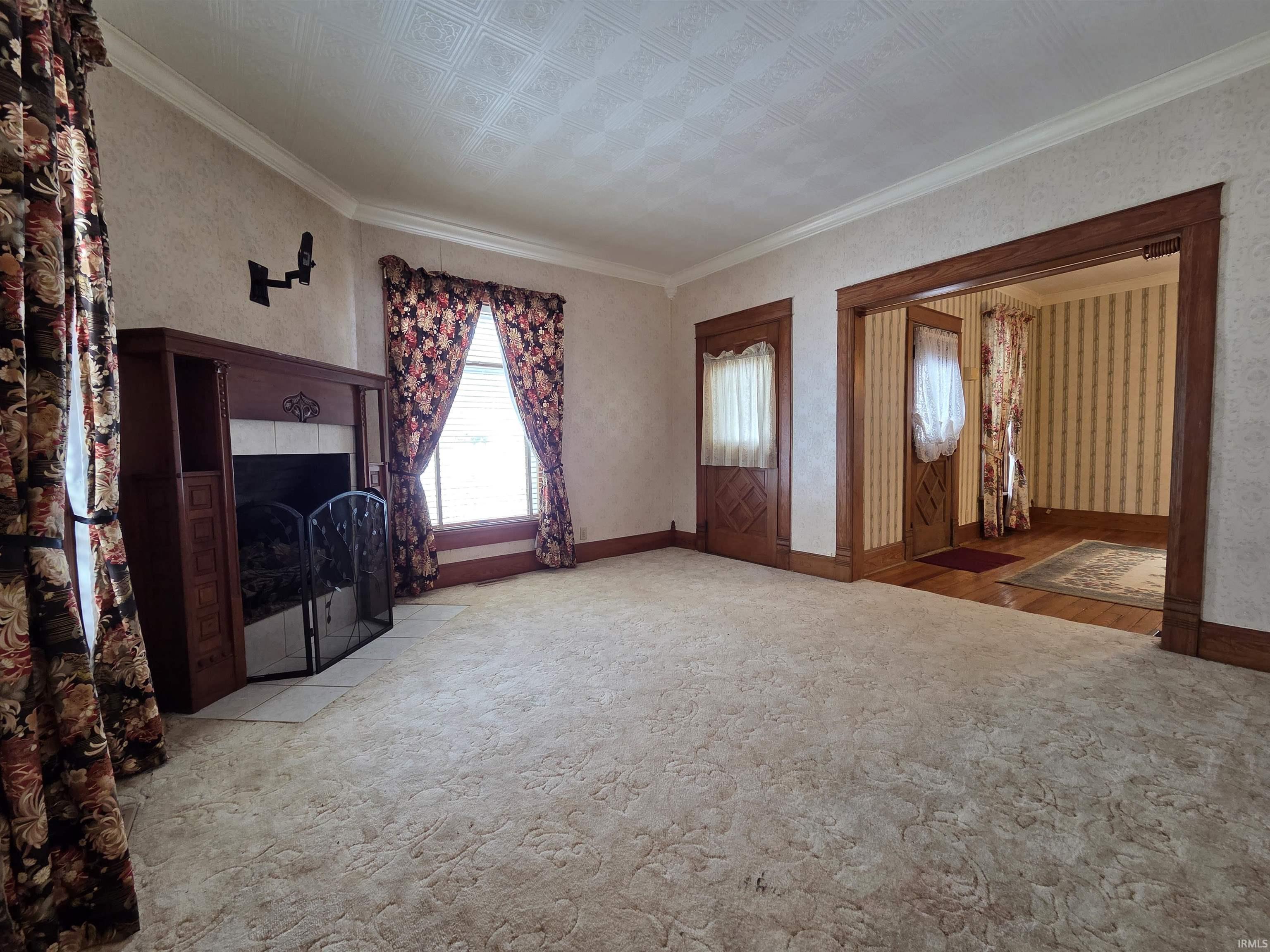 Unfurnished living room featuring an ornate ceiling, carpet flooring, ornamental molding, and wallpapered walls