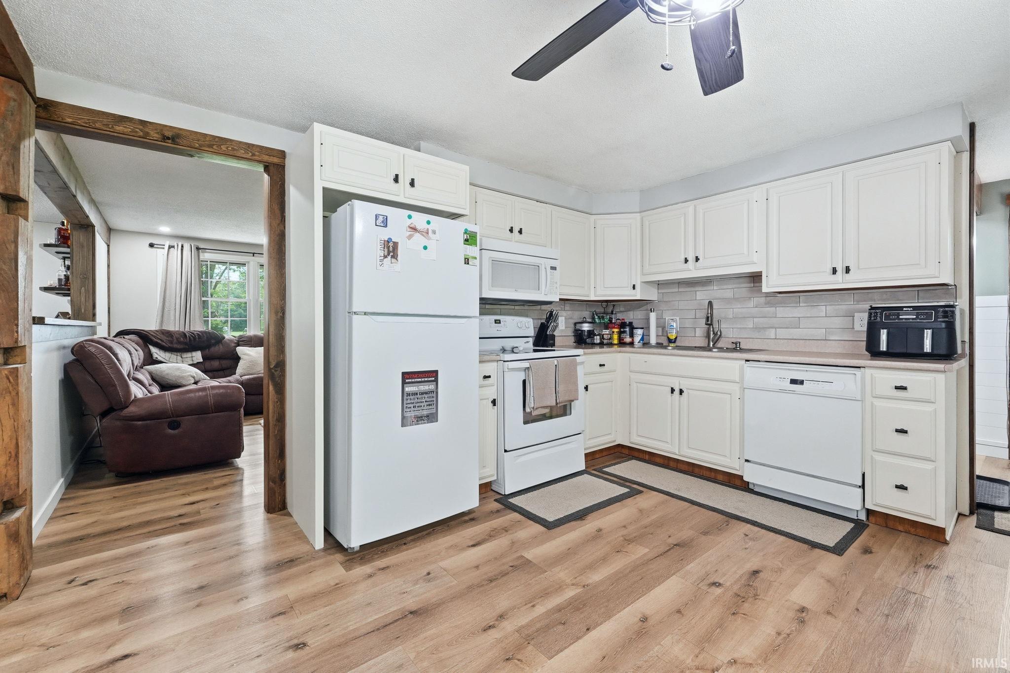 Kitchen featuring light wood-finish flooring, white cabinetry, integrated white appliances, and a tiled backsplash
