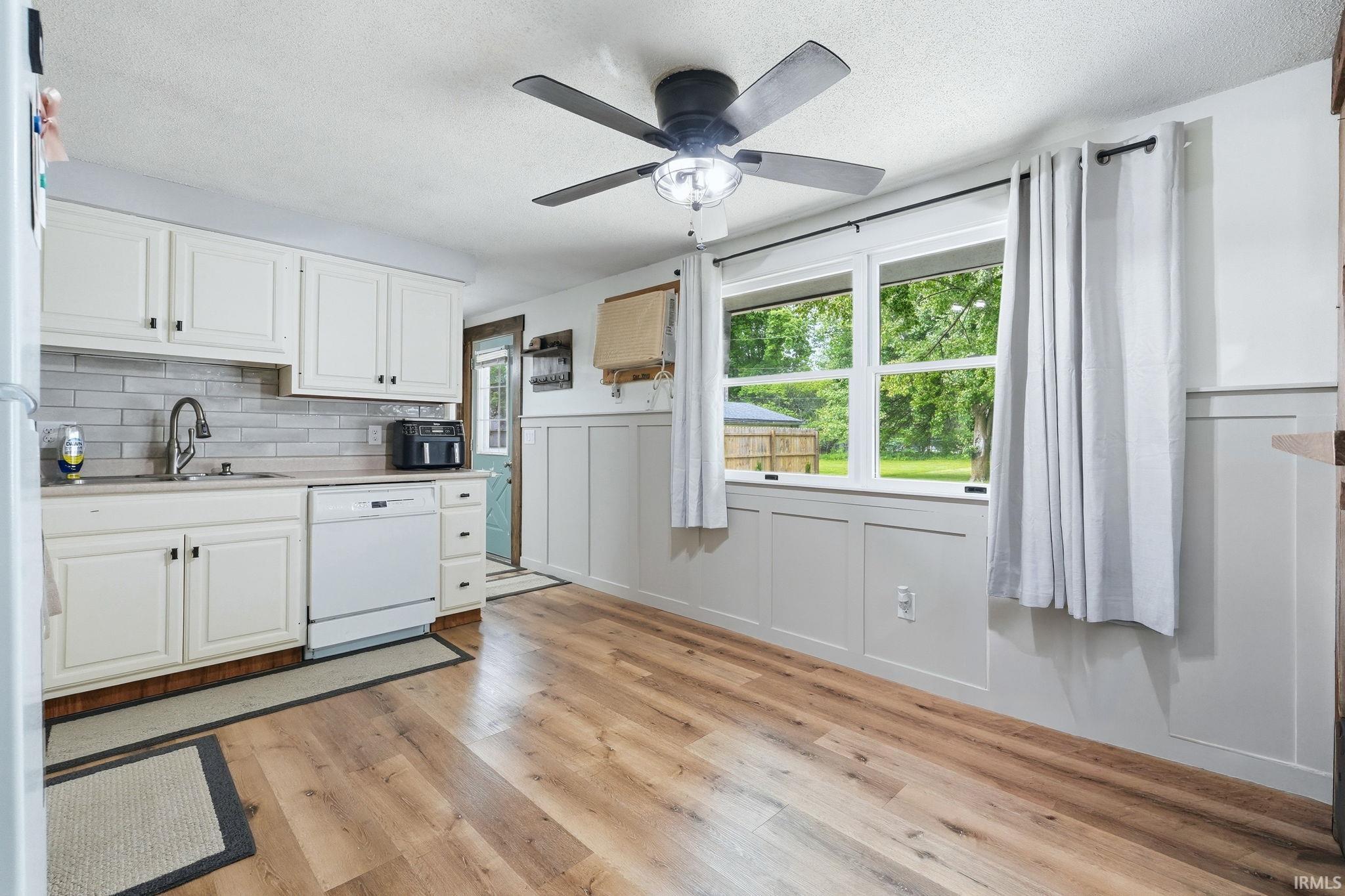 Kitchen area featuring wood-finish flooring, white cabinetry, and a tile backsplash