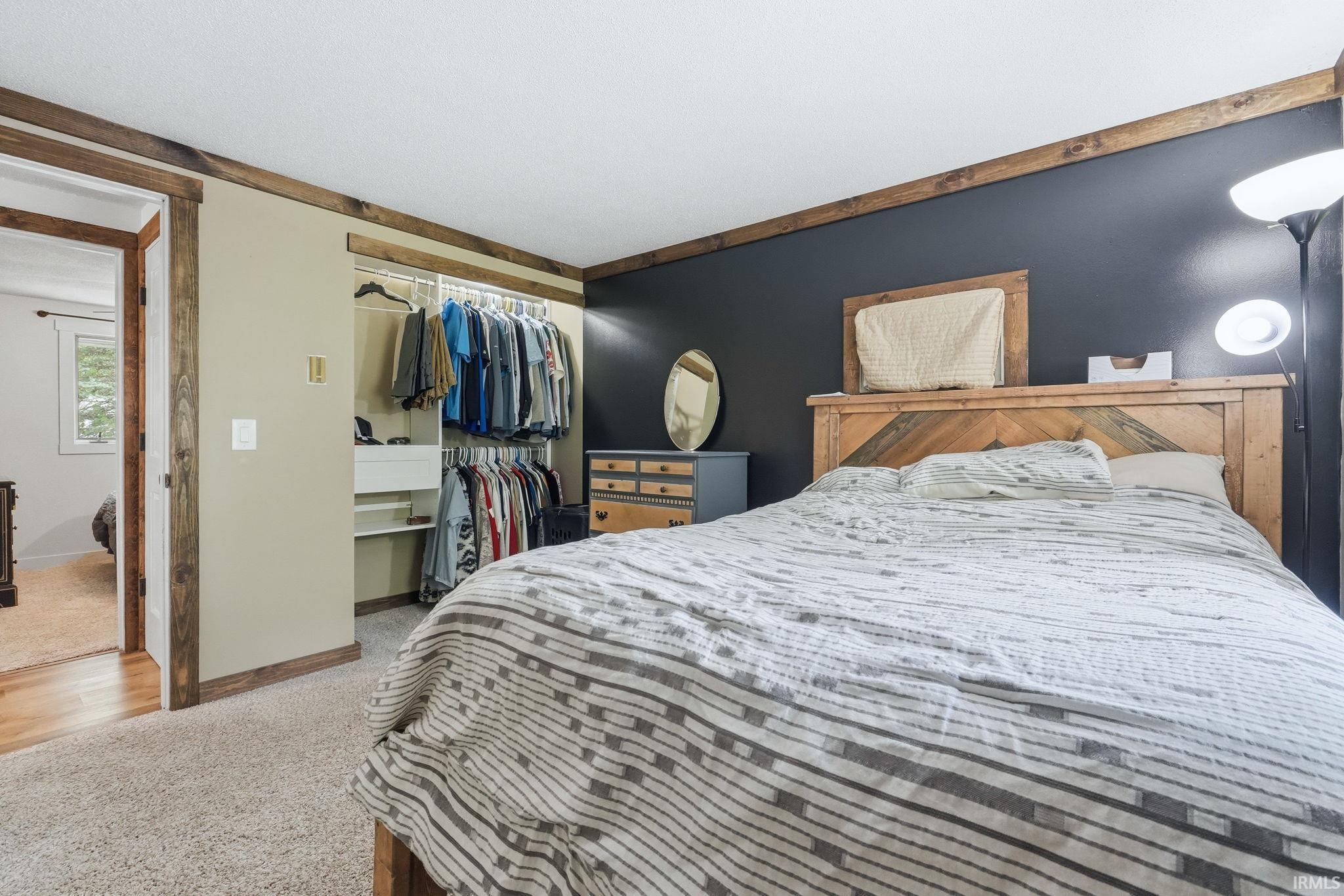 Bedroom featuring textured carpeting, an open closet system with shelving, a dark accent wall, and wood-finish trim