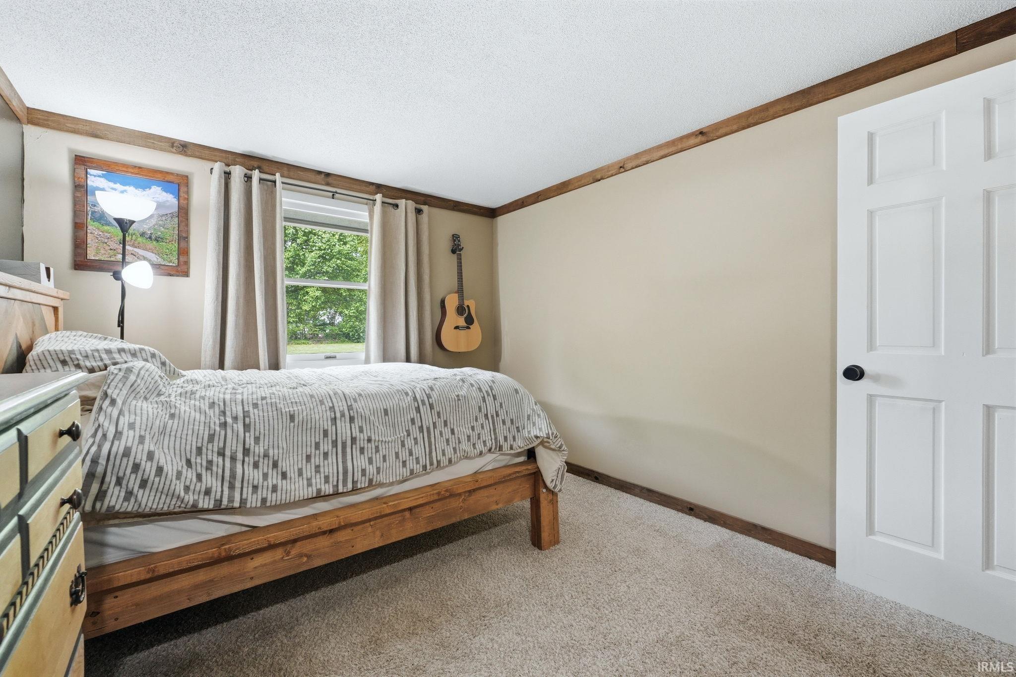 Carpeted interior room featuring a single window, a six-panel interior door, baseboard trim, crown molding, and neutral wall paint