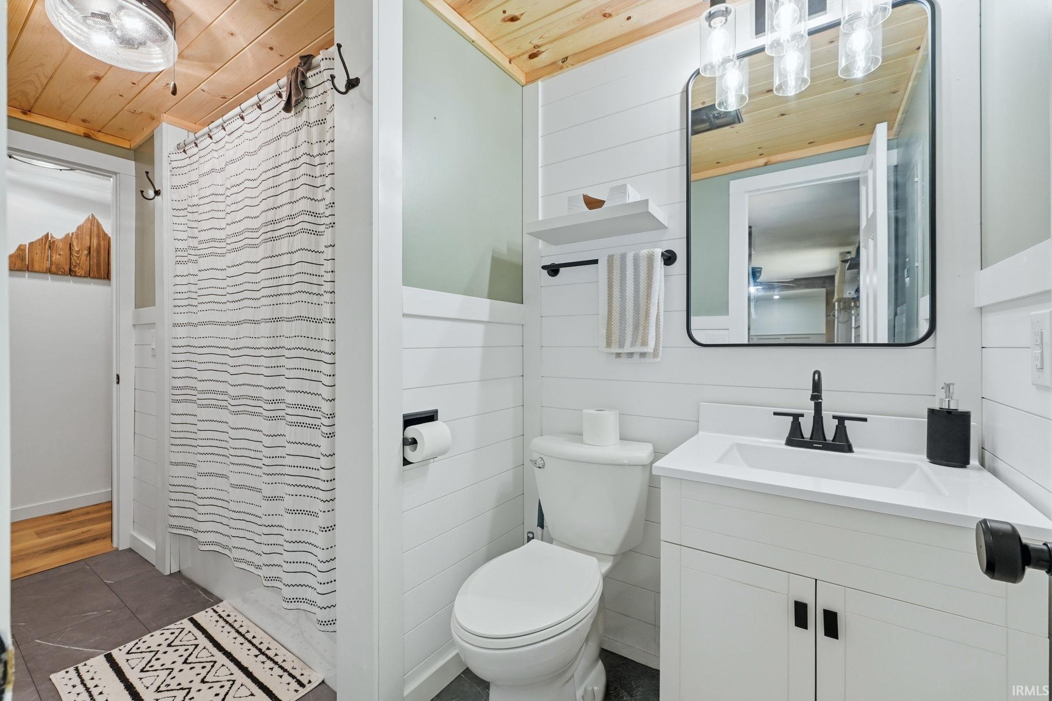 Bathroom featuring shiplap walls, wood-finish ceiling, dark tile flooring, a single vanity with storage, and a shower with a privacy curtain