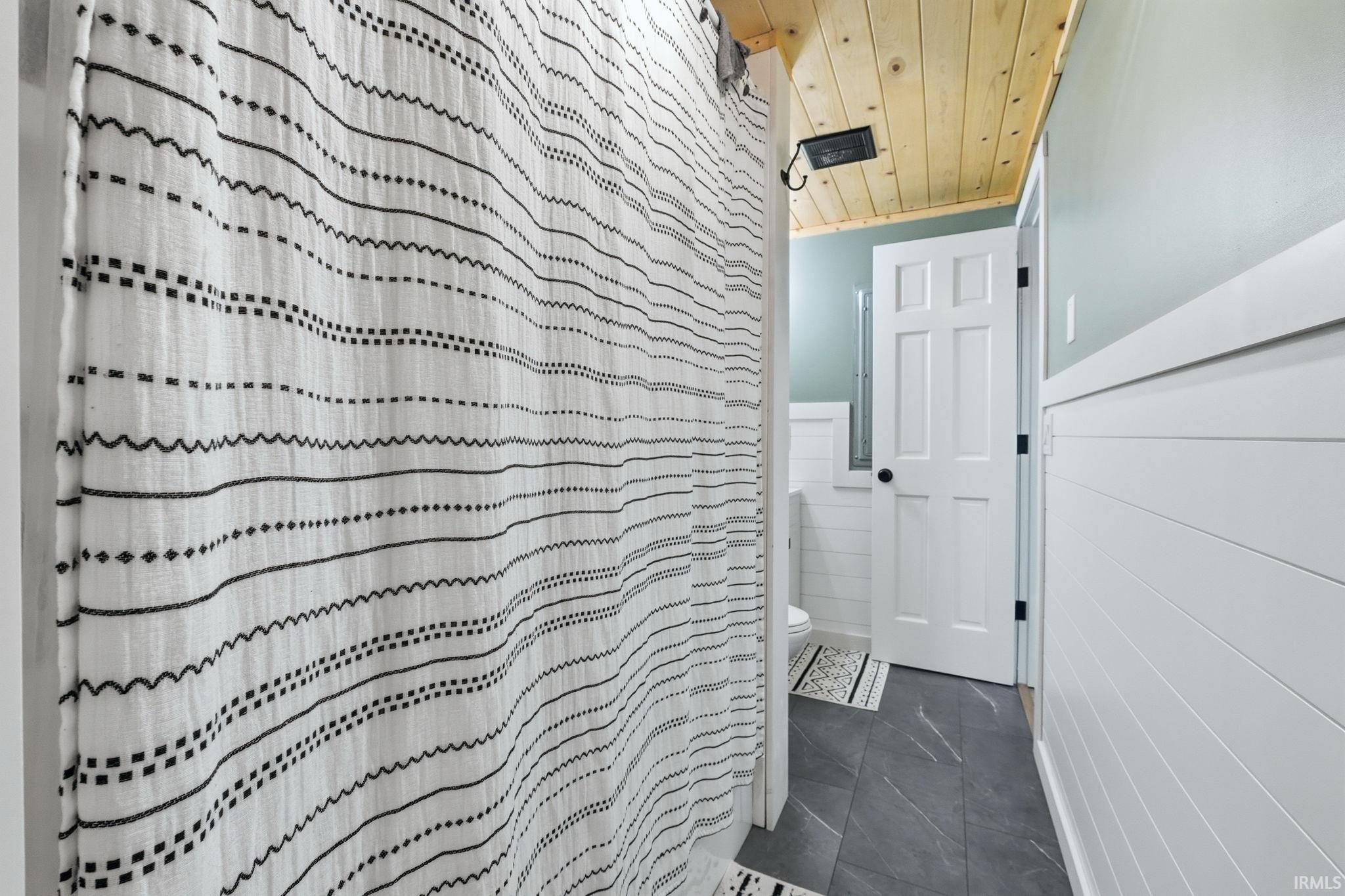 Bathroom featuring ship-lap wall paneling, a wood-paneled ceiling, dark floor tiling, and a crisp white door with black hardware