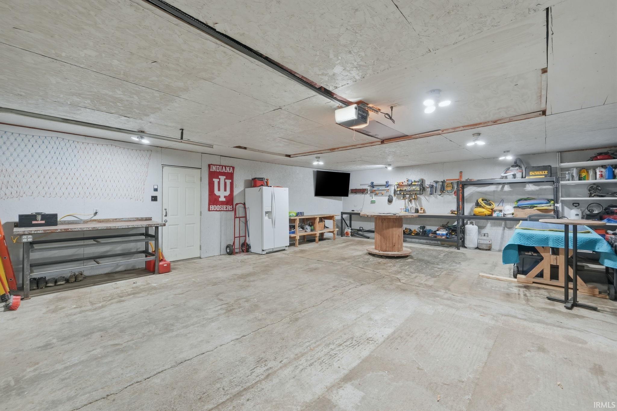 Spacious garage featuring a concrete floor, overhead garage door opener, multiple wall-mounted lights, and ample workspace