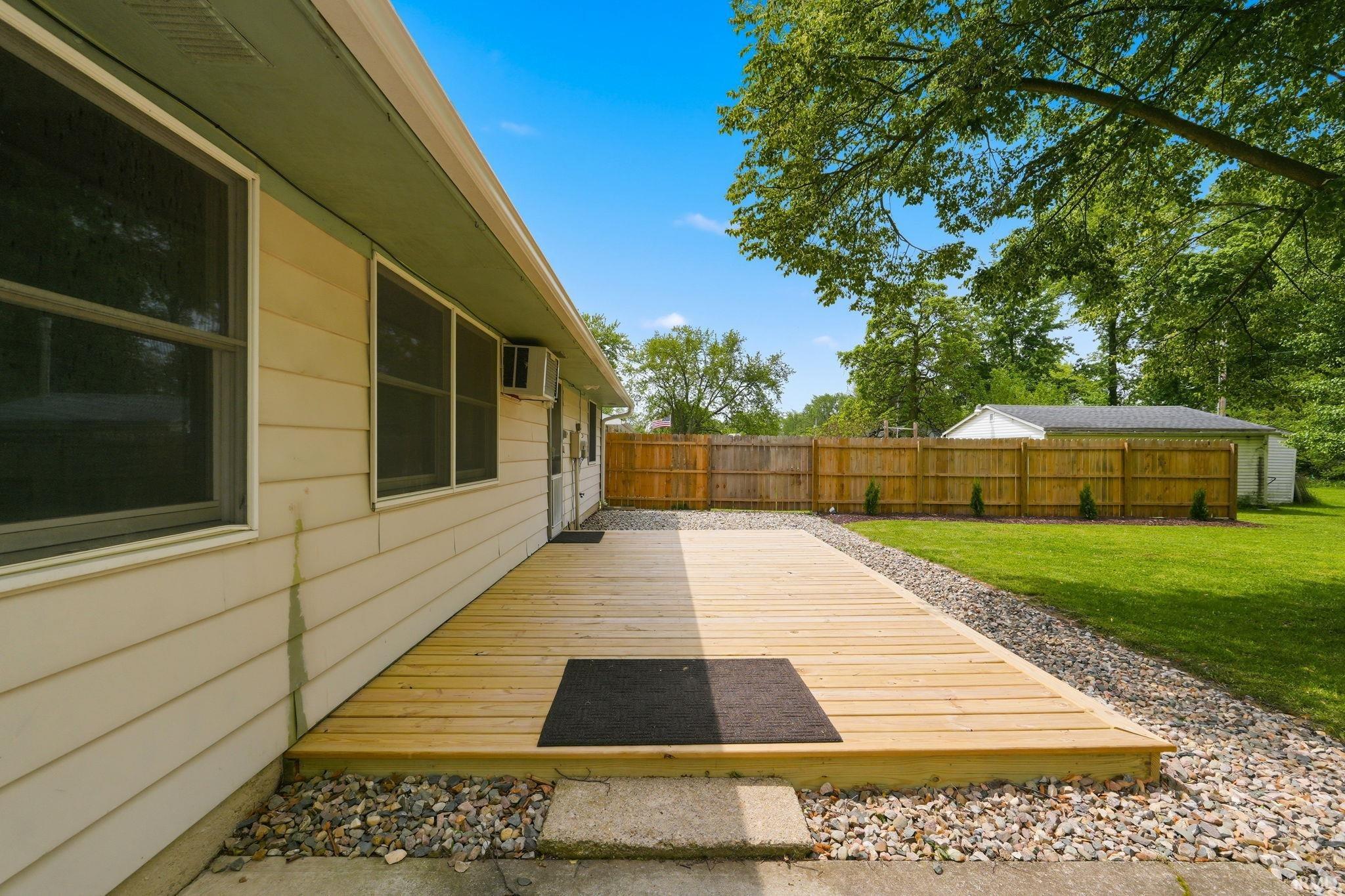 Expansive backyard featuring a new wood deck, gravel landscaping, a privacy fence, and a spacious lawn