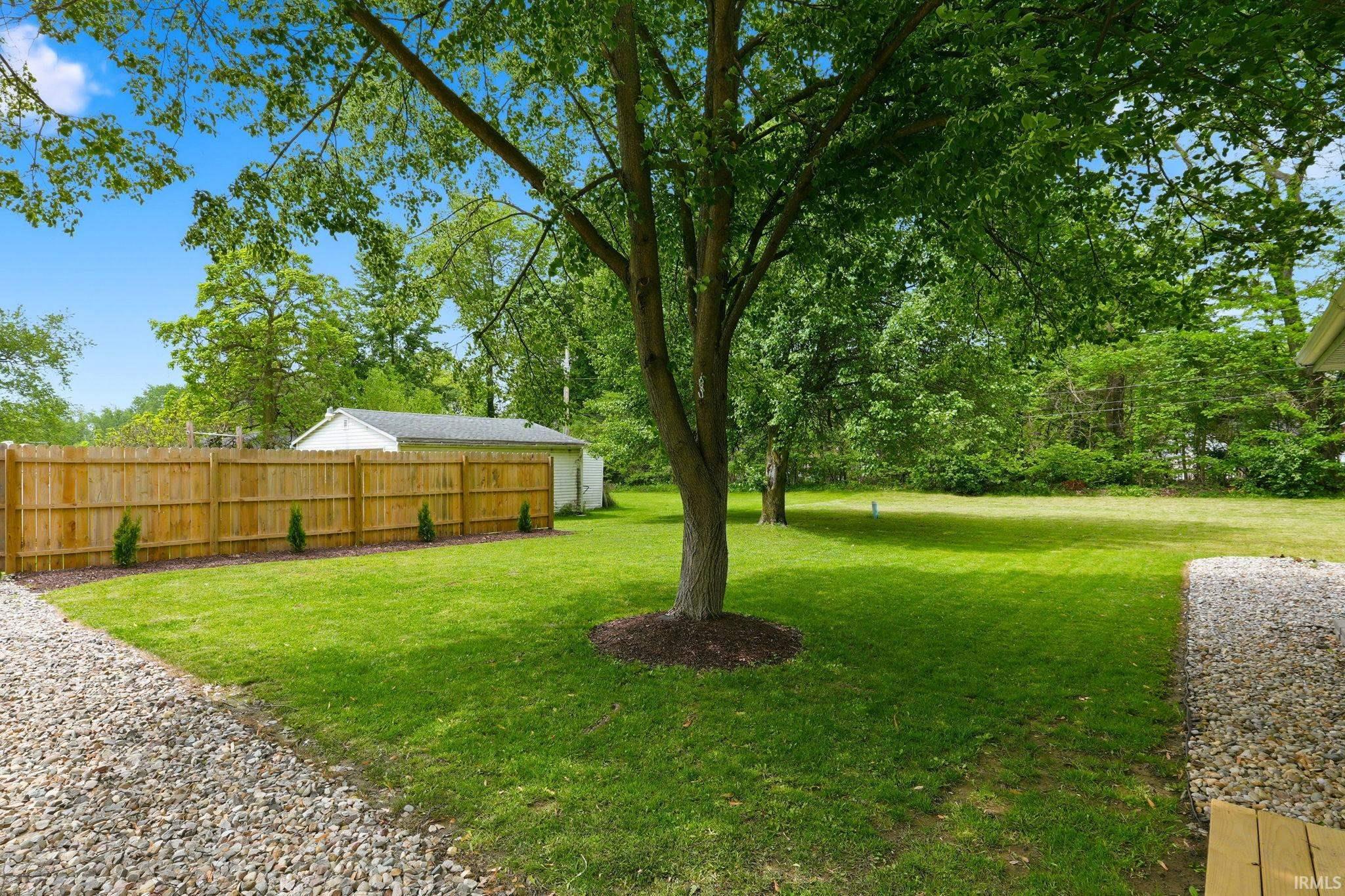 Expansive backyard featuring a large tree, manicured lawn, and natural wood privacy fencing
