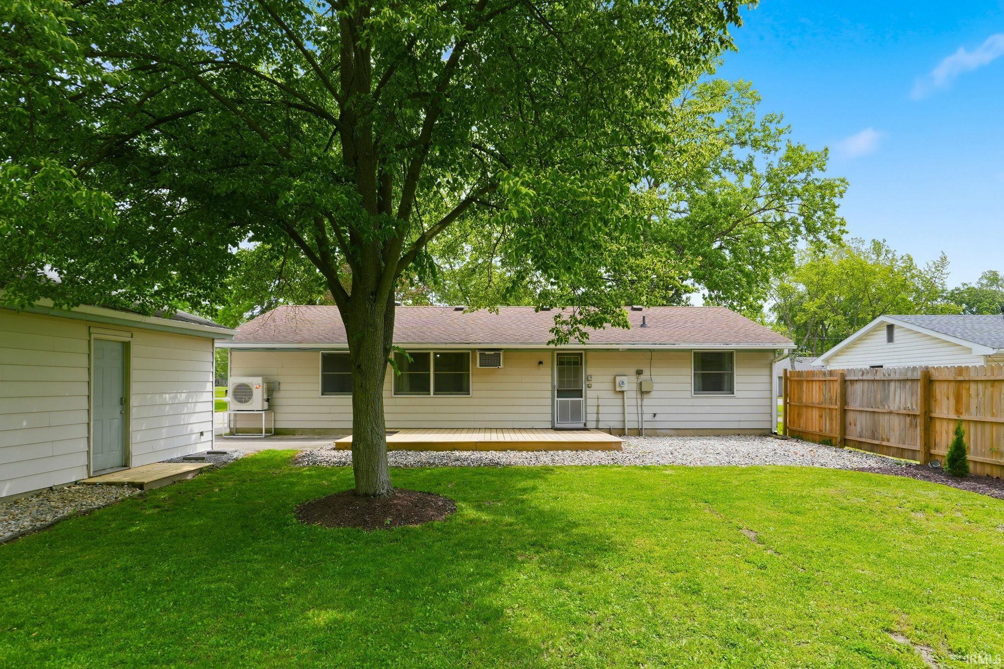 Expansive rear yard featuring a wooden privacy fence, mature shade tree, and a wooden deck