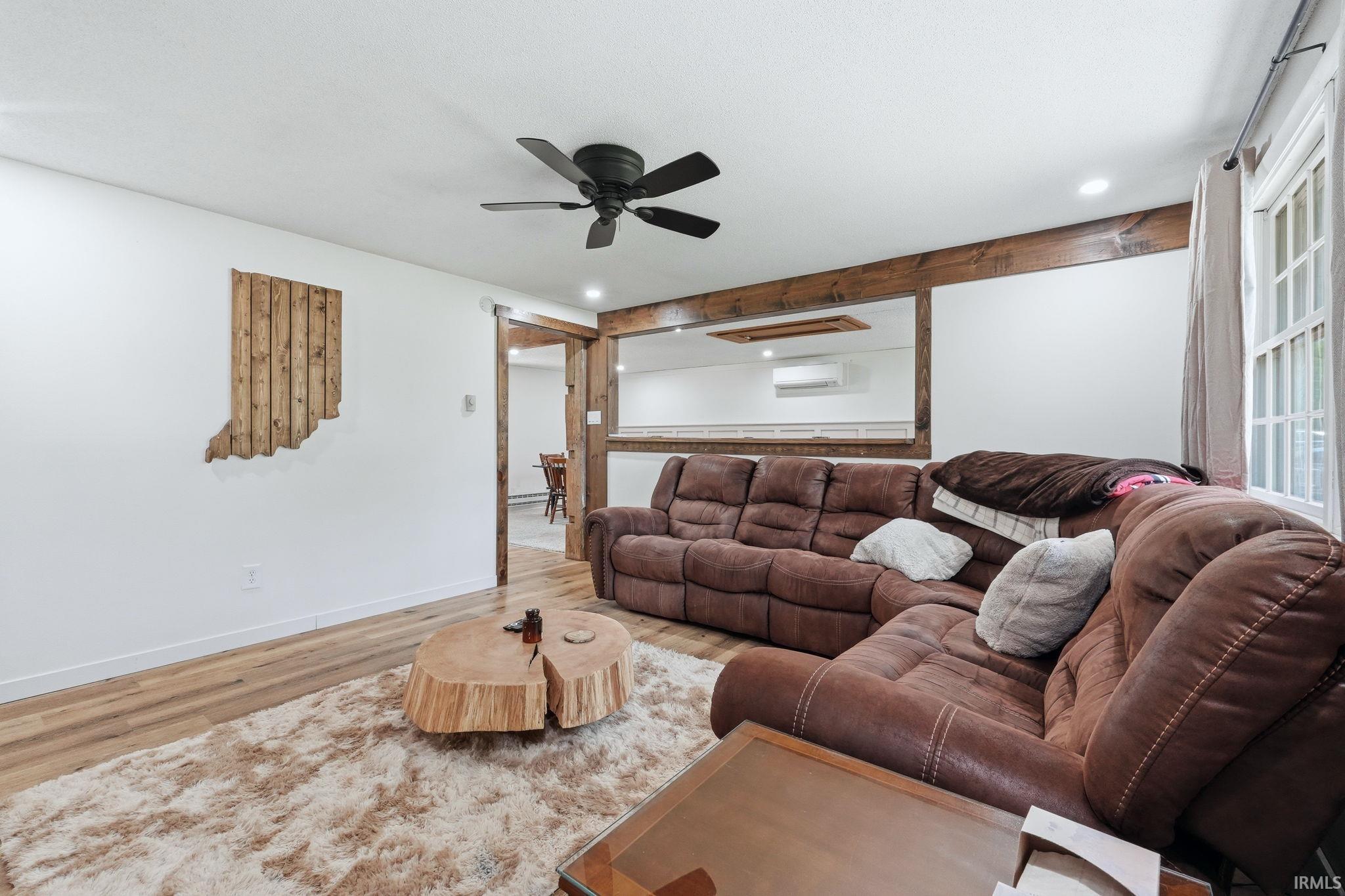 Living area featuring wood-finish flooring, white walls, and a black ceiling fan