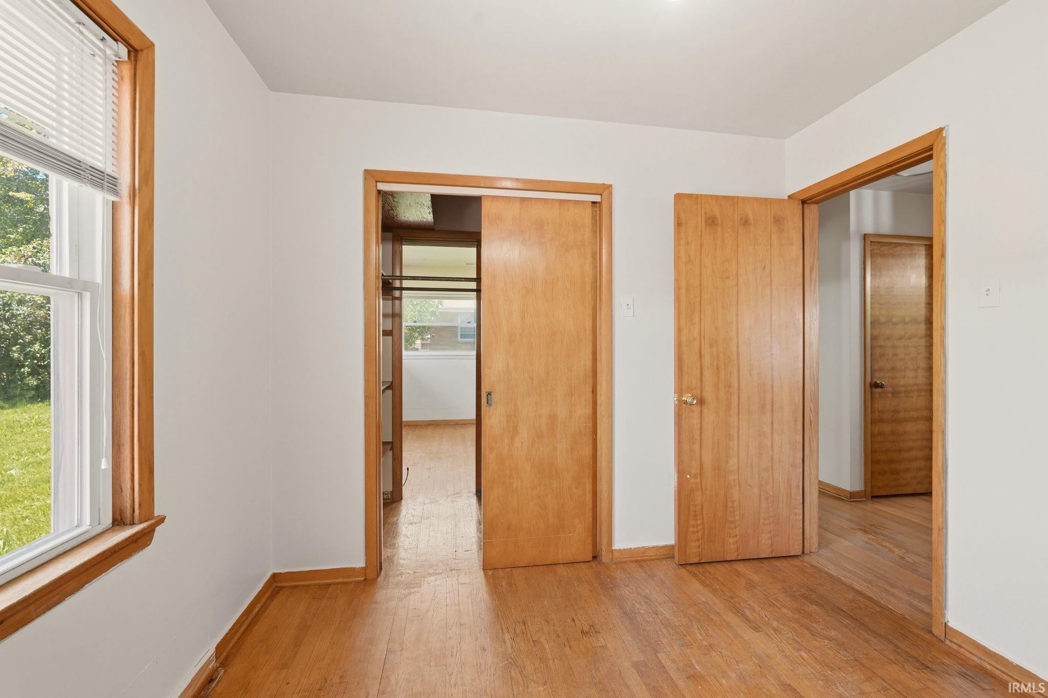 Room featuring wood-finish flooring, white walls, and a window with blinds